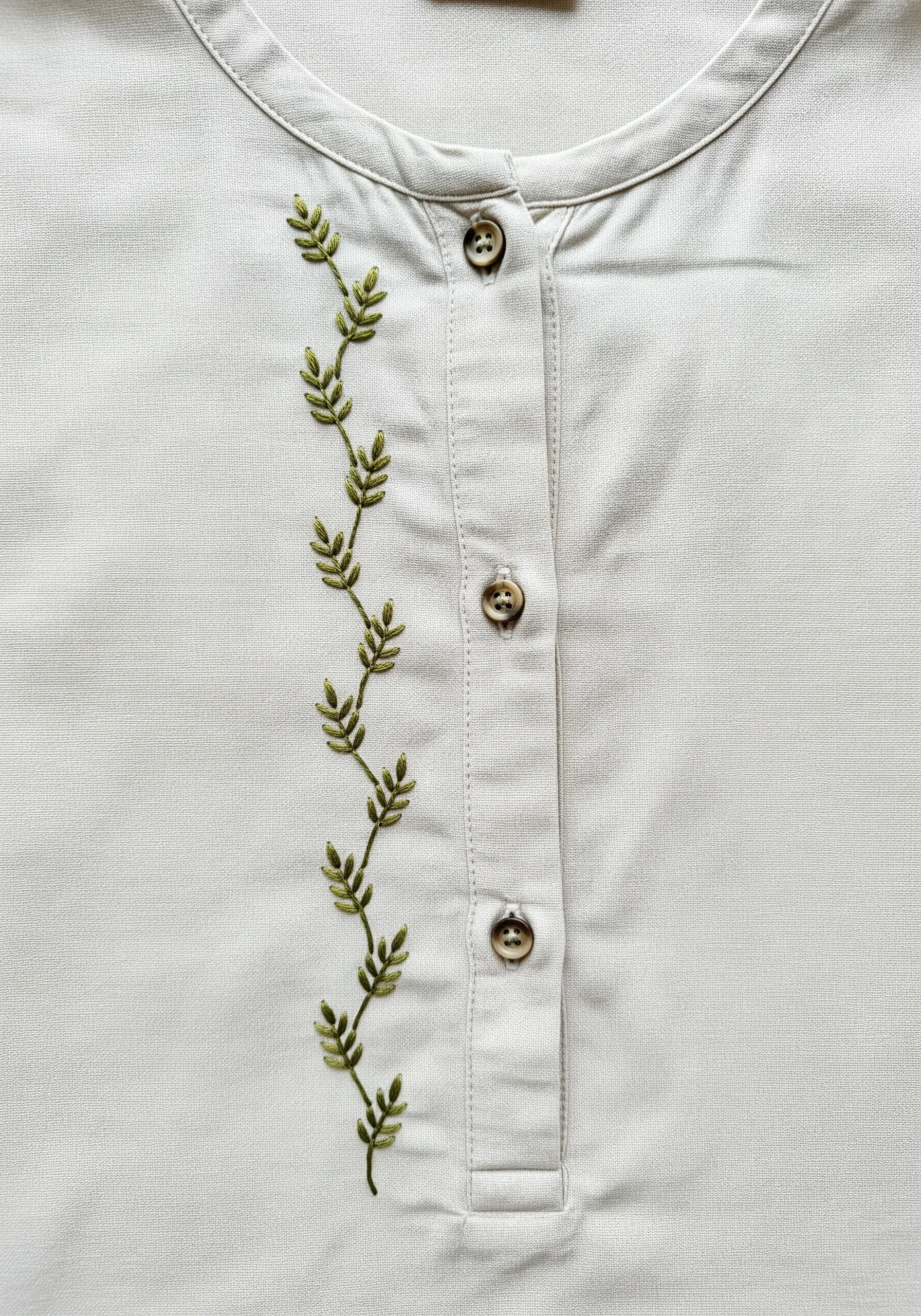 An embroidered green vine with small leaves trailing down a shirt's button placket.