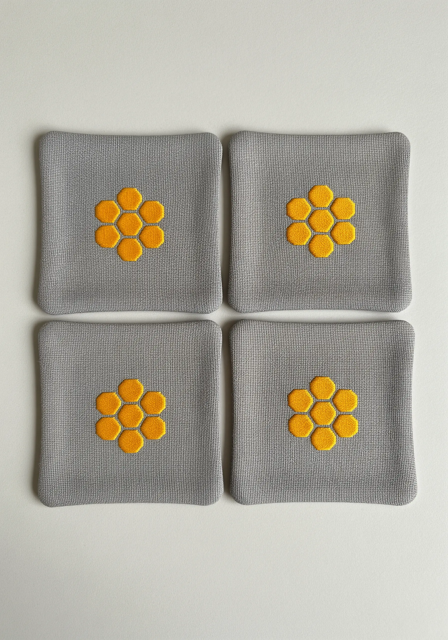 Yellow honeycomb pattern embroidered on a set of four grey fabric coasters.