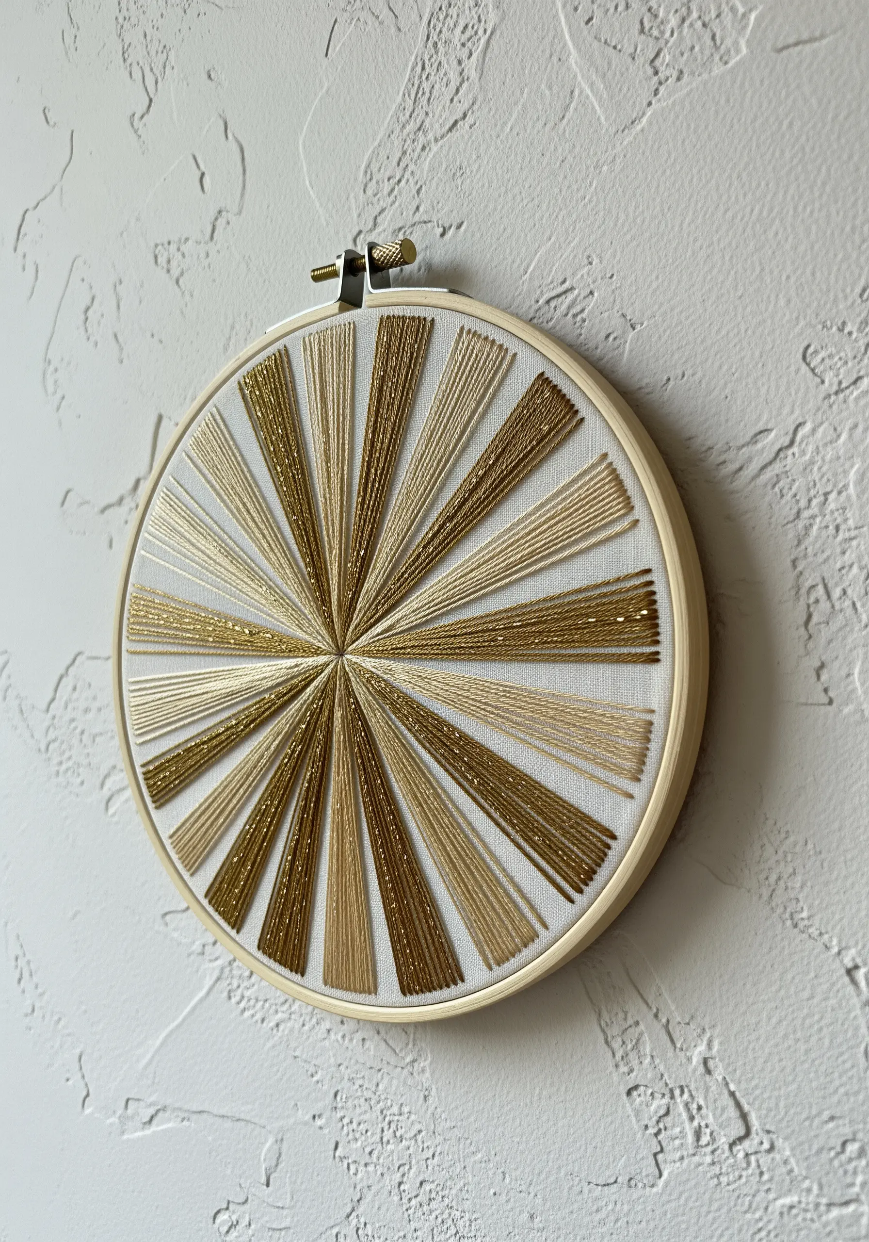 A geometric sunburst pattern in a hoop using alternating gold metallic threads.