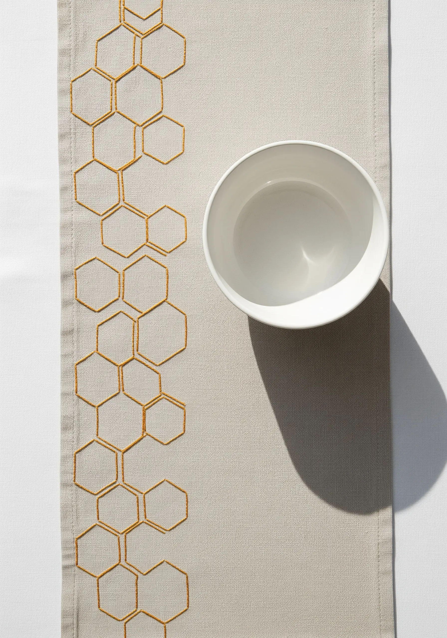 A honeycomb pattern embroidered in gold thread along the edge of a table runner.
