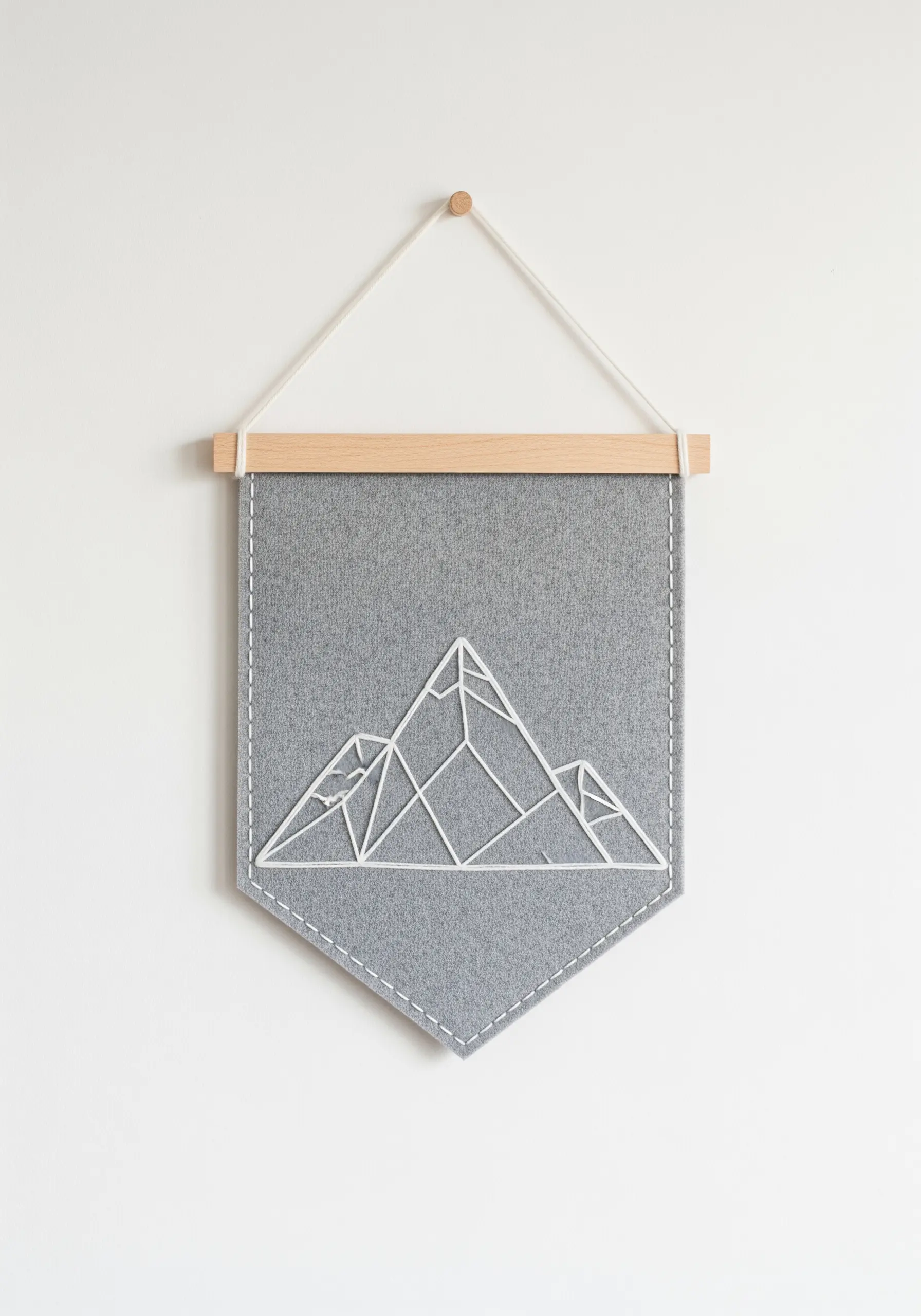 A grey felt wall banner with a geometric mountain outline stitched in thick white thread.