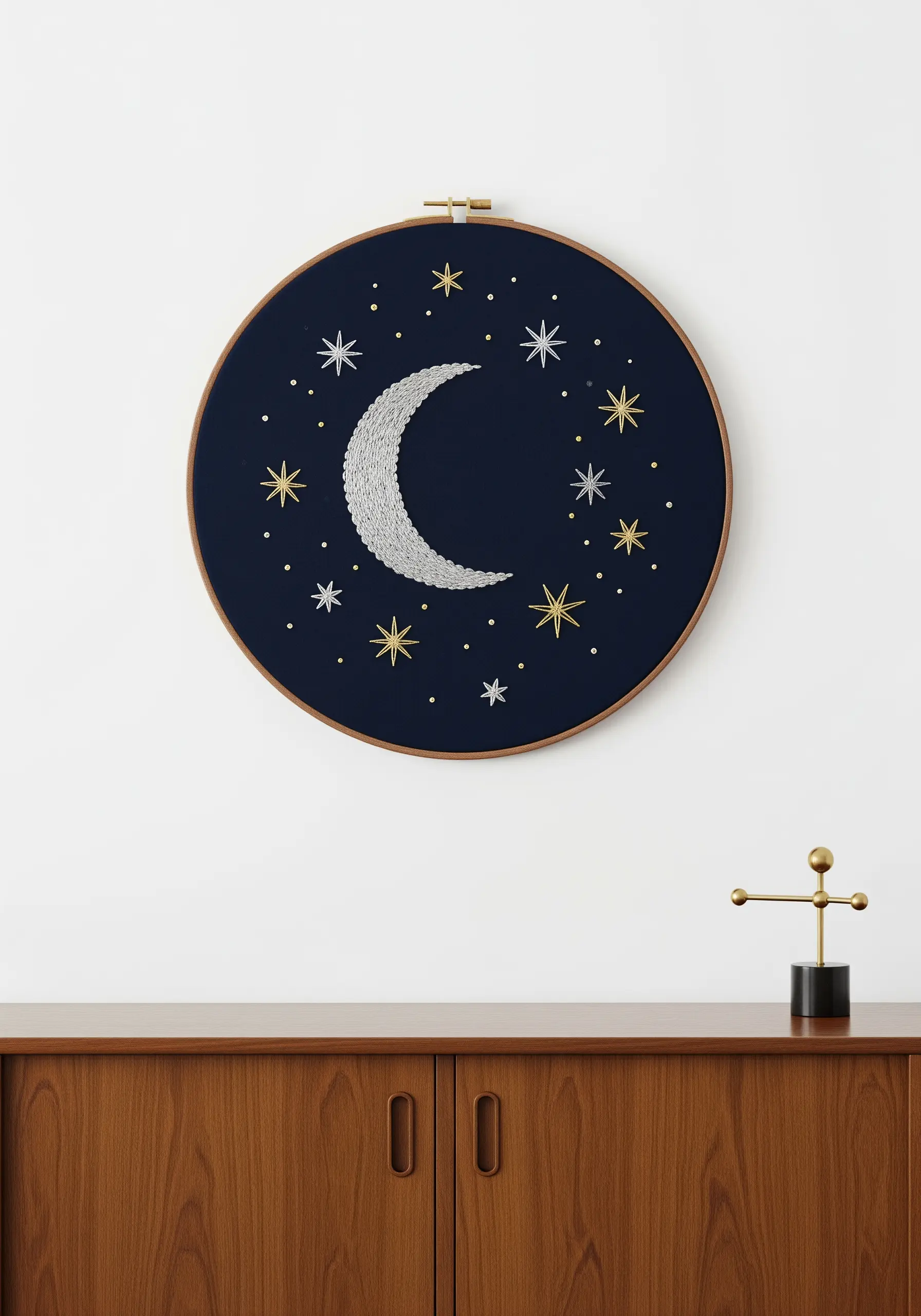 Embroidery of a silver crescent moon and gold and silver stars on dark navy fabric.