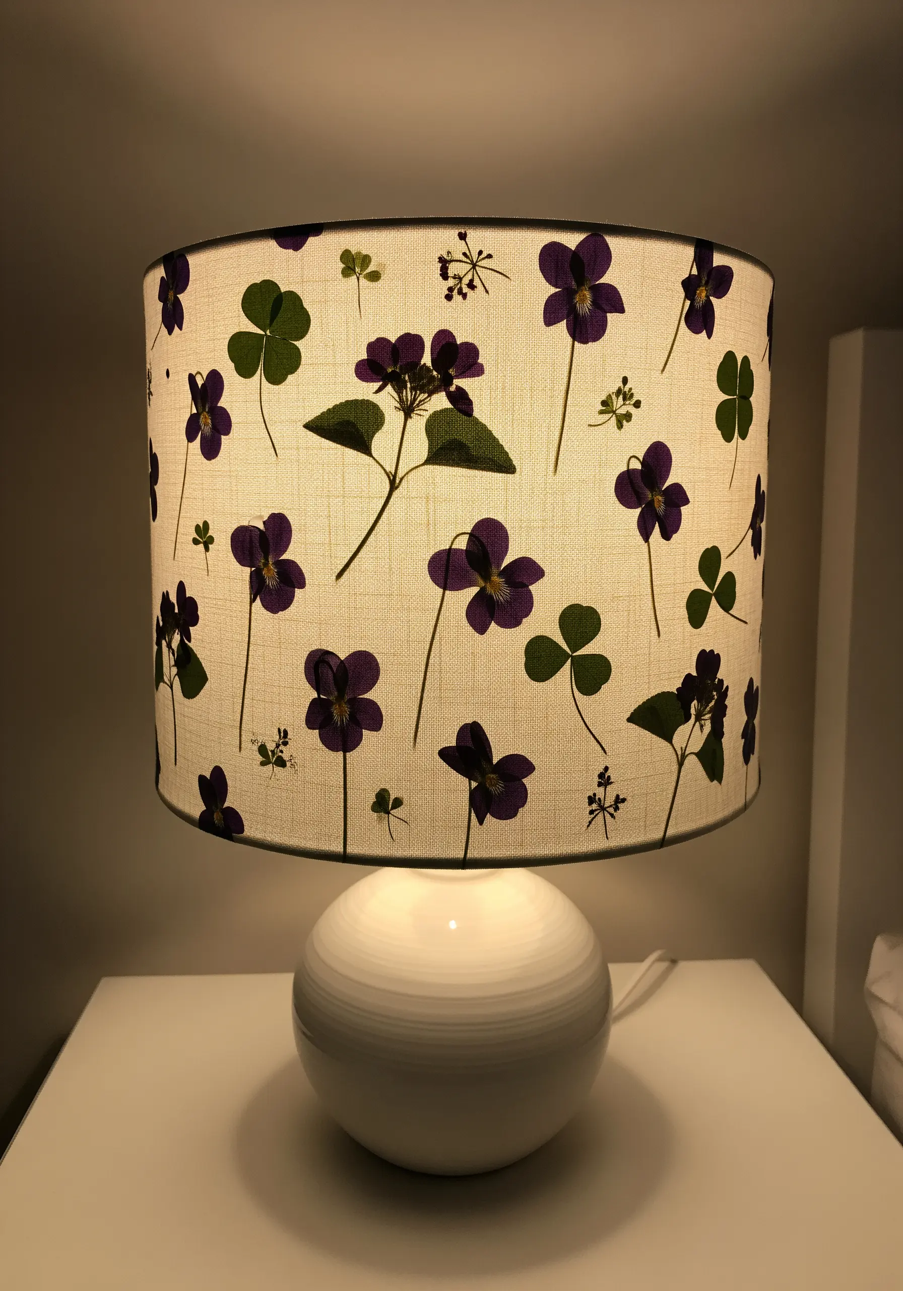 A drum lampshade decorated with a pattern of pressed purple violets and green clover leaves.