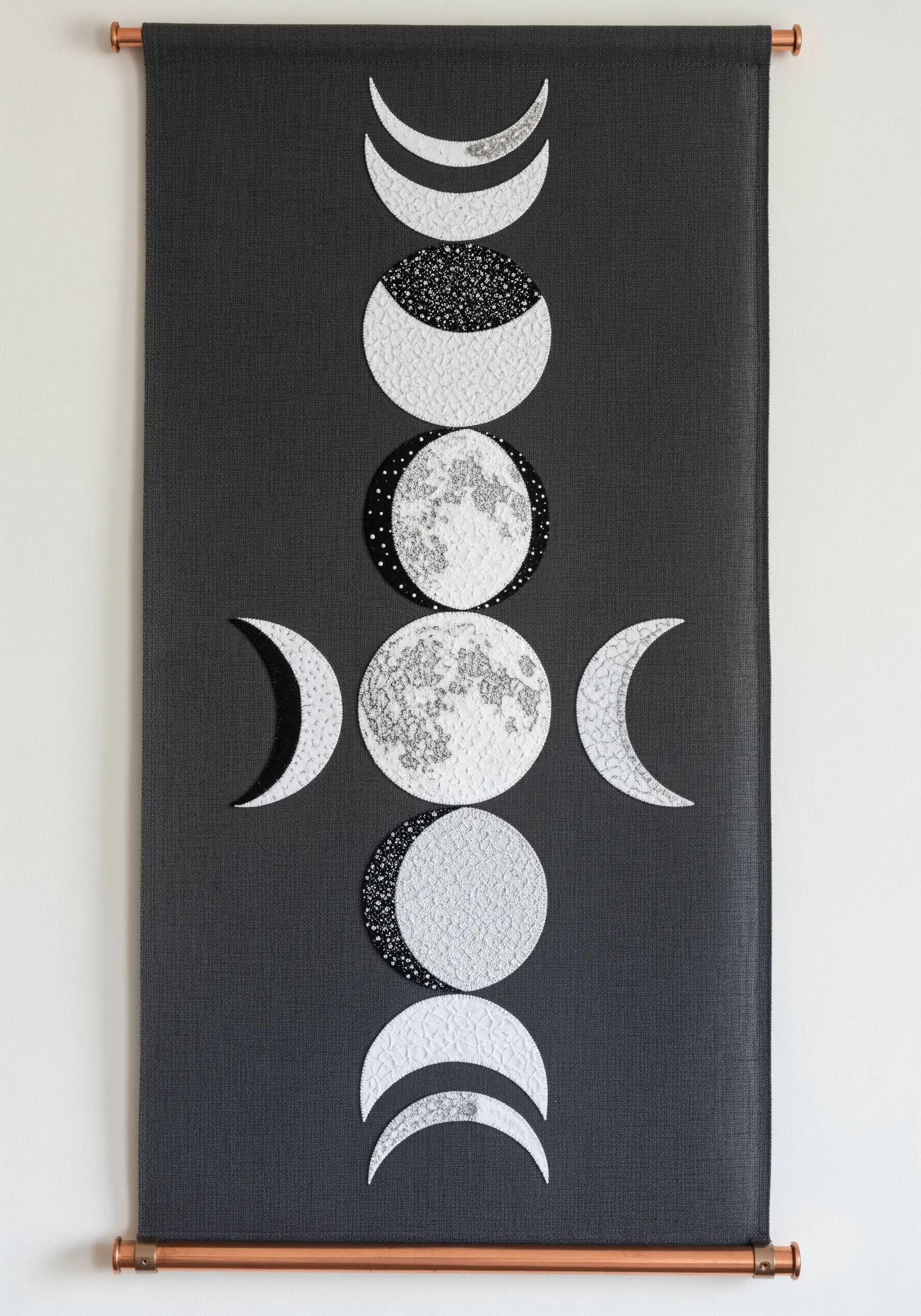A dark grey wall banner showing the phases of the moon made from textured fabric appliqué.