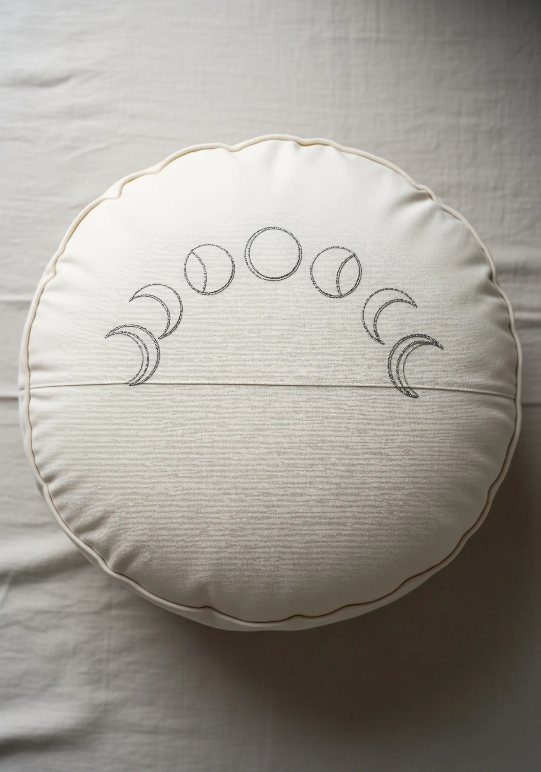 Moon phases embroidered in an arc on a round white cushion, with textured fill.