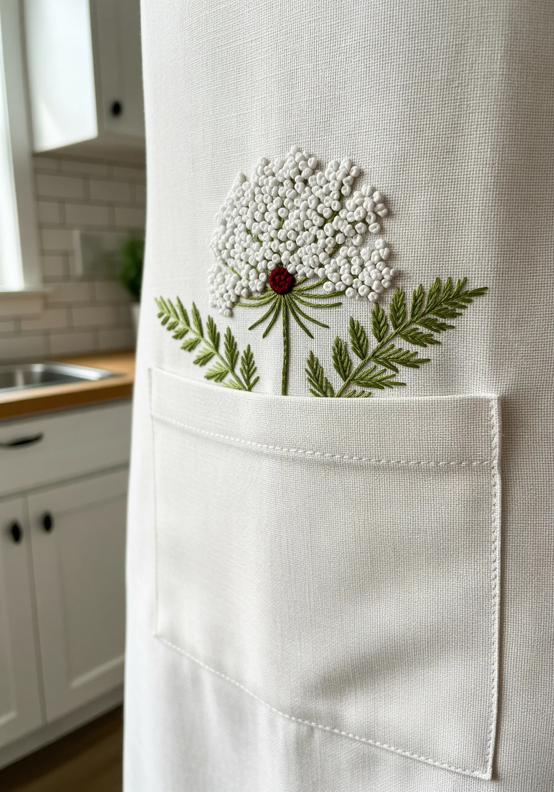 A Queen Anne's Lace embroidery motif emerging from the pocket of a linen apron.