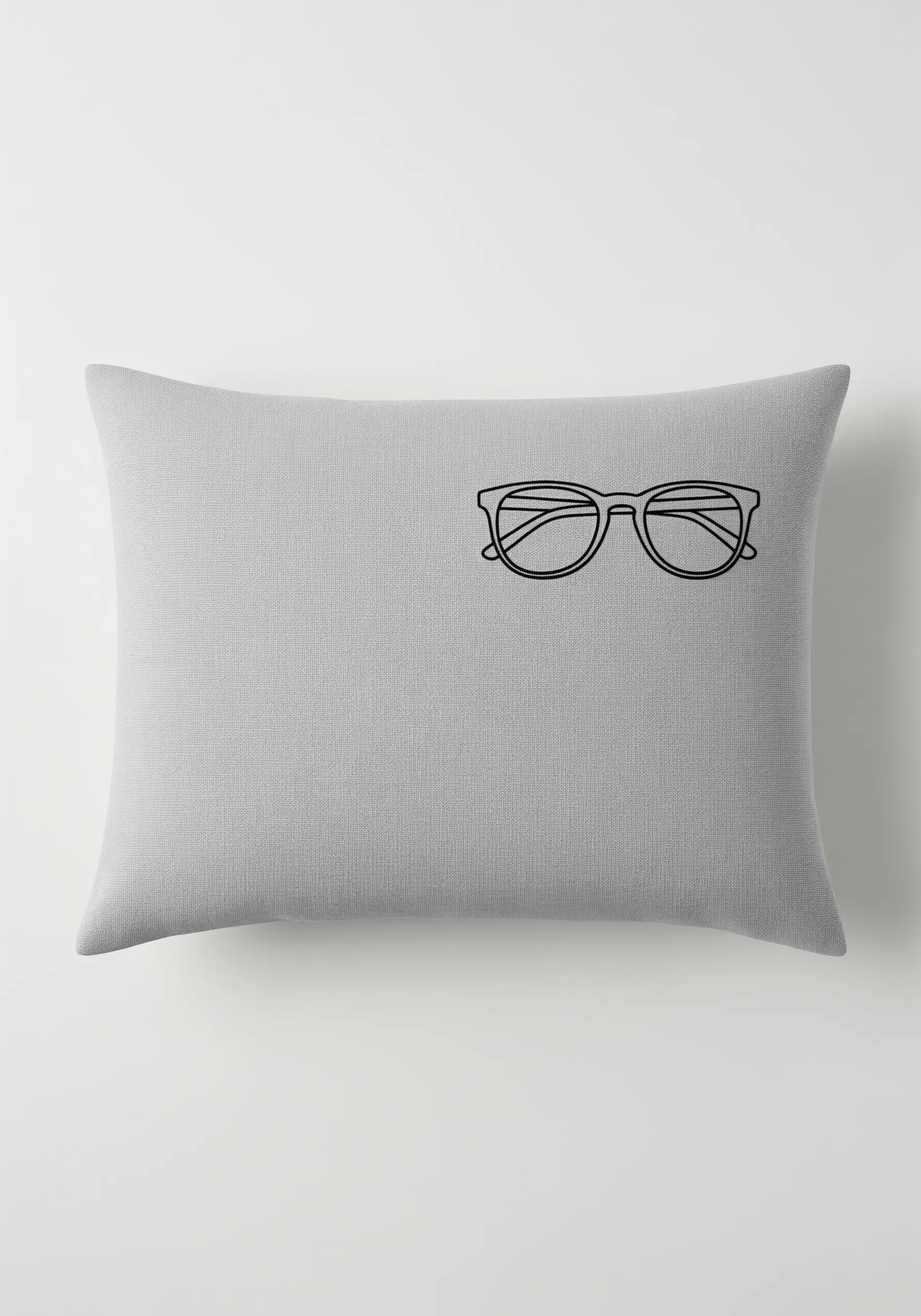 A small, off-center embroidered pair of glasses on a large grey rectangular cushion.