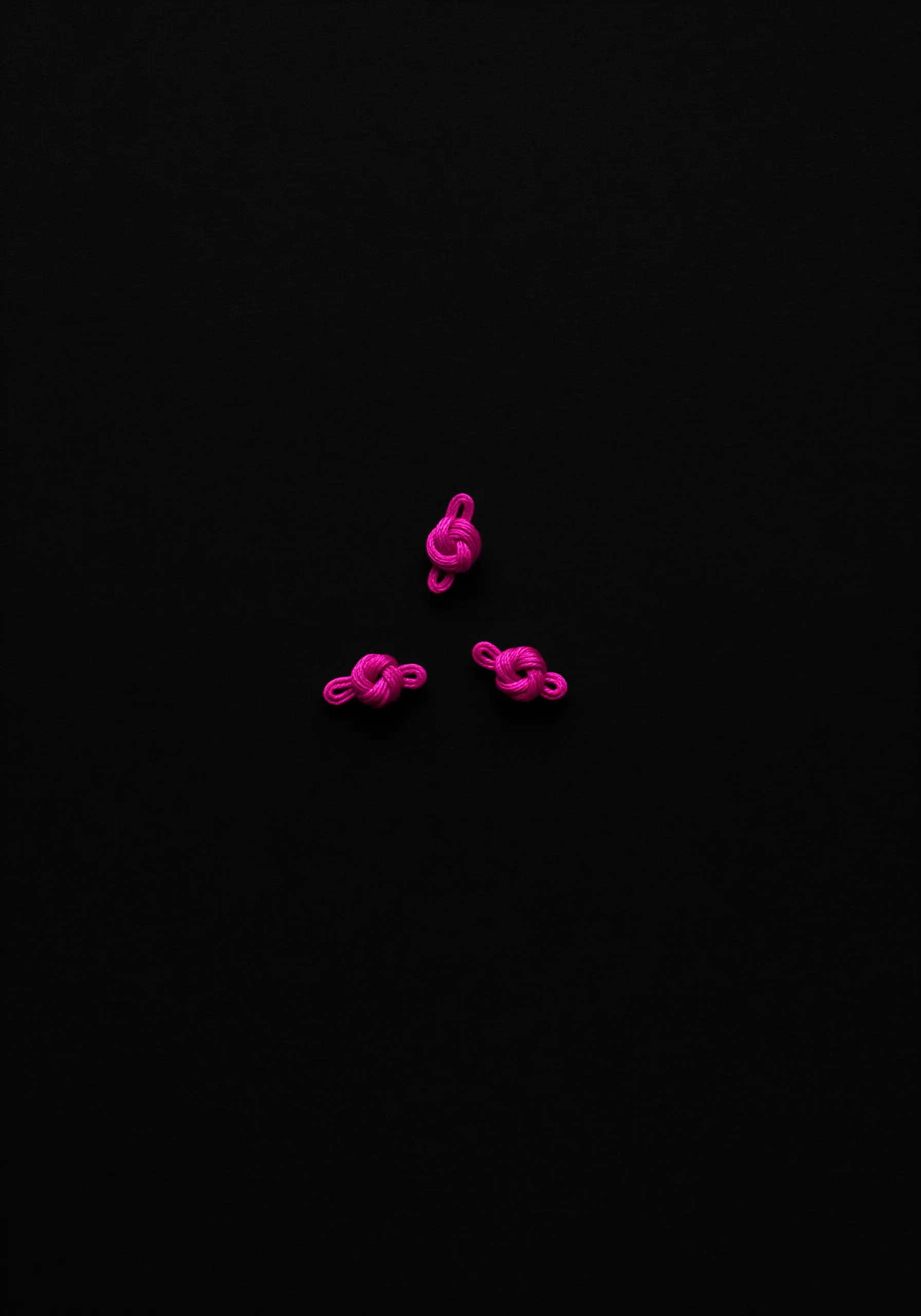 Three small, intricate pink embroidery knots arranged on a solid black background.