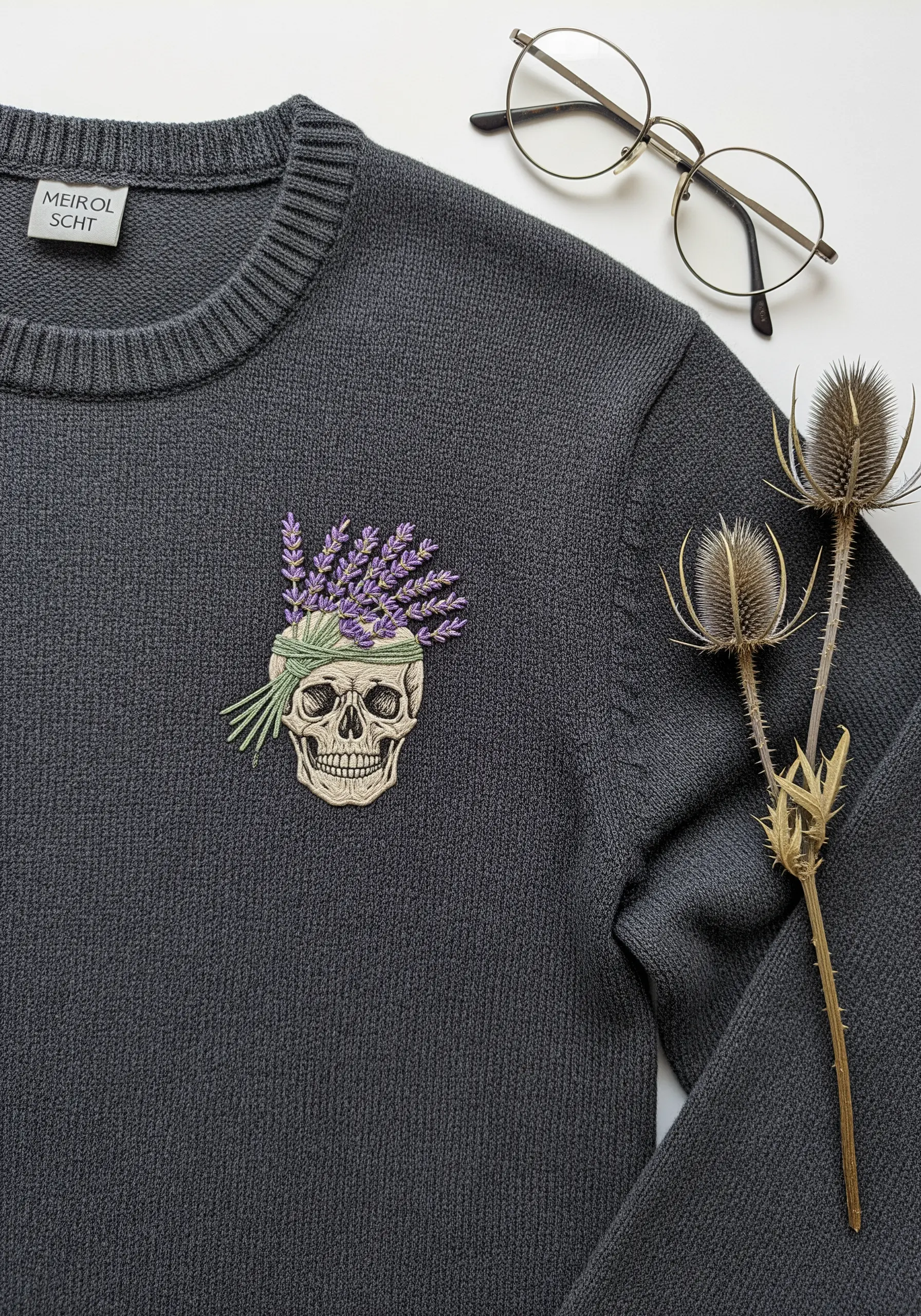 Embroidered skull with a bouquet of lavender on its crown, stitched on a charcoal gray sweater.