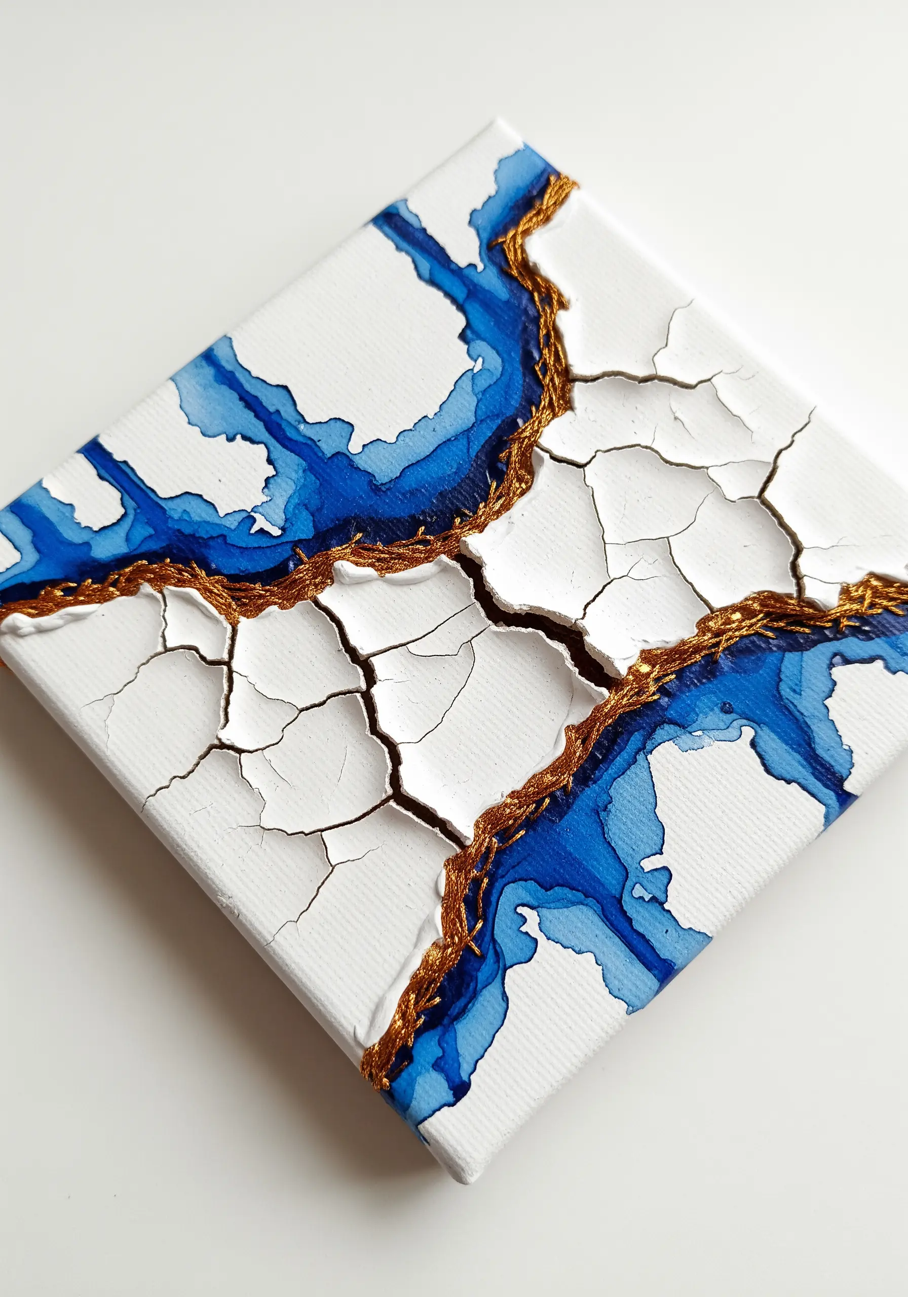 Gold thread embroidered into the fissures of white crackle paste on canvas.