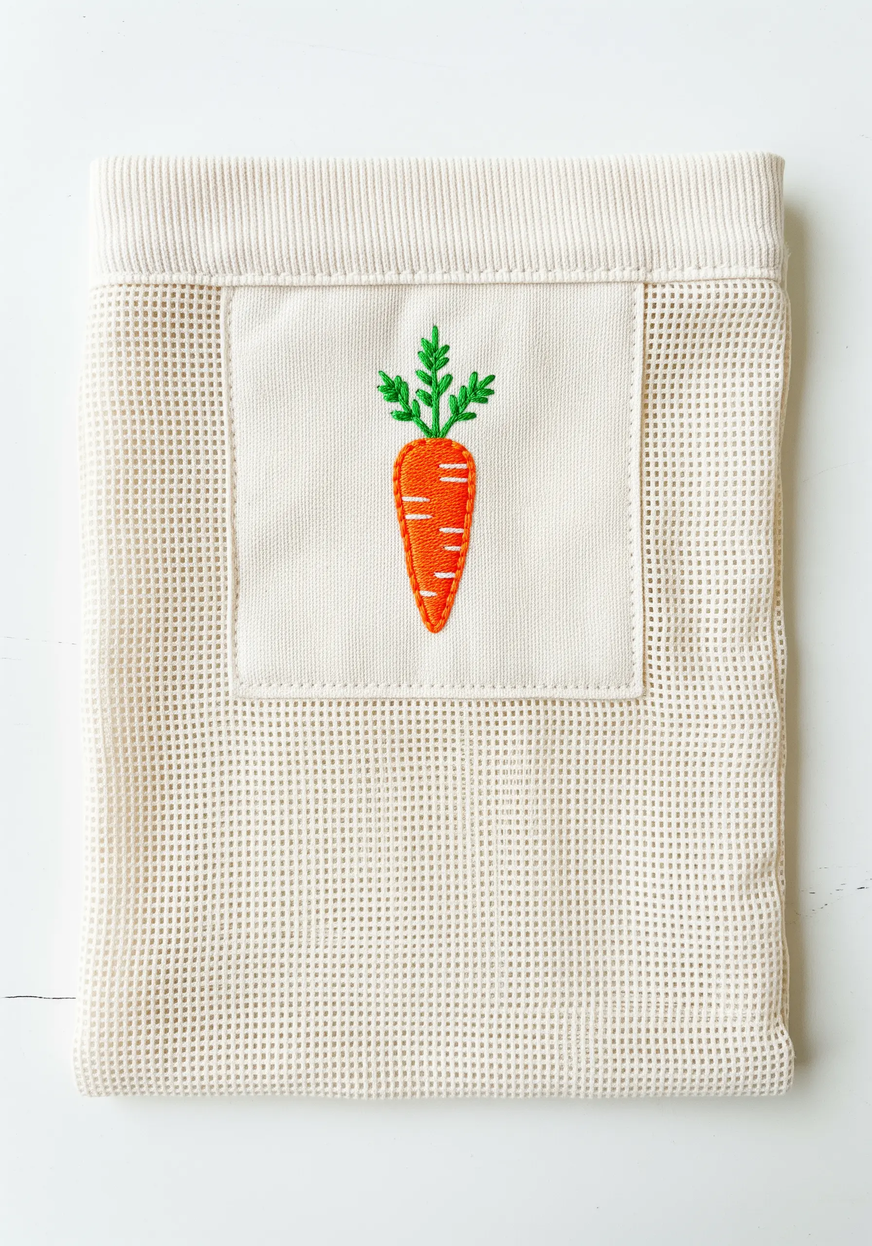 An embroidered carrot on a canvas patch sewn onto a mesh produce bag.