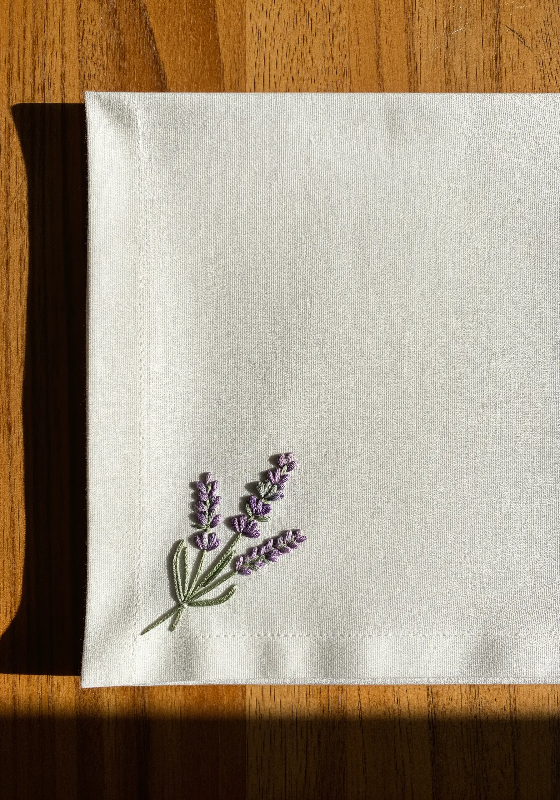 Hand-embroidered lavender sprig with French knots on a white linen napkin.
