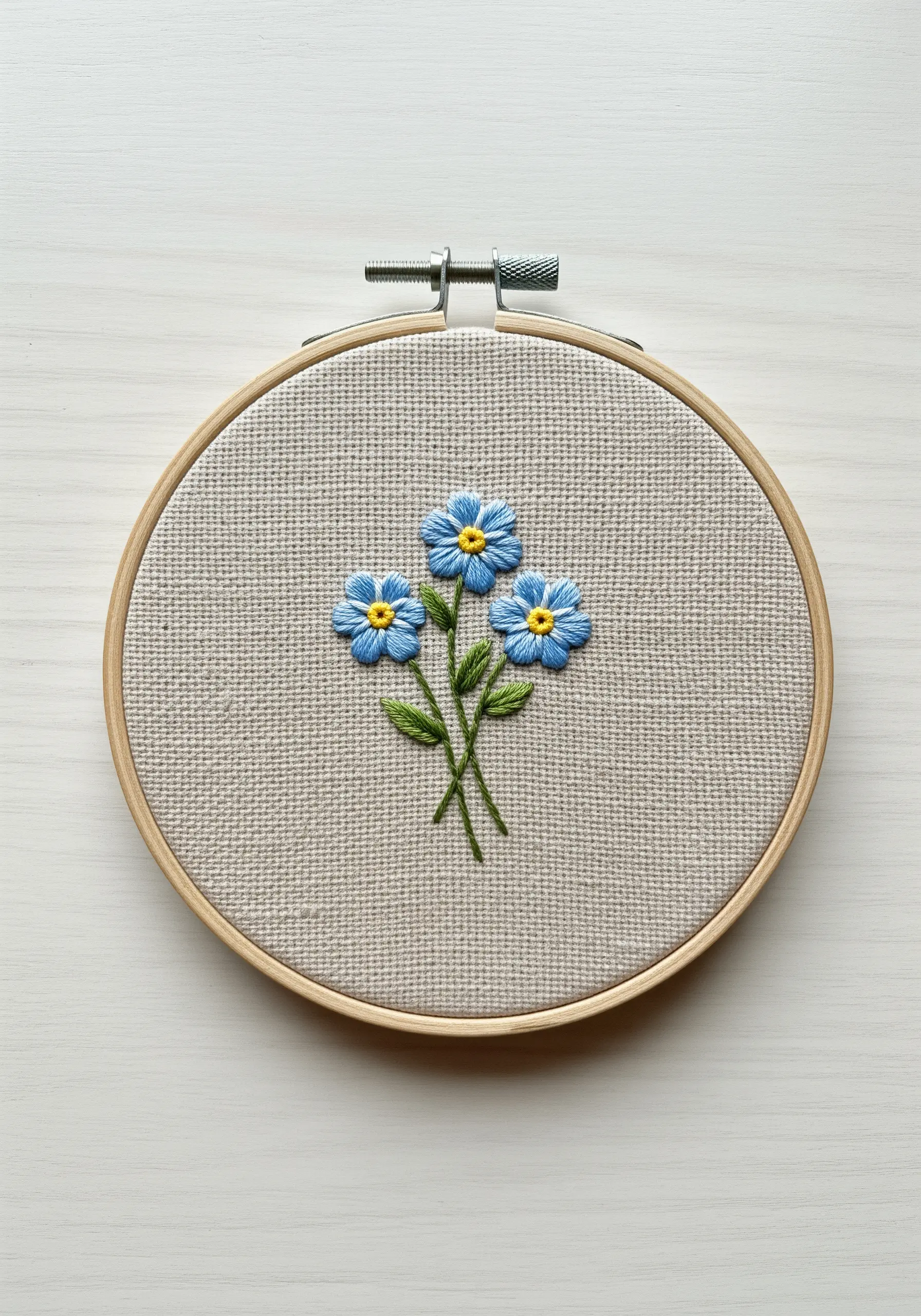 Three blue forget-me-not flowers created with layered lazy daisy stitches and yellow centers.