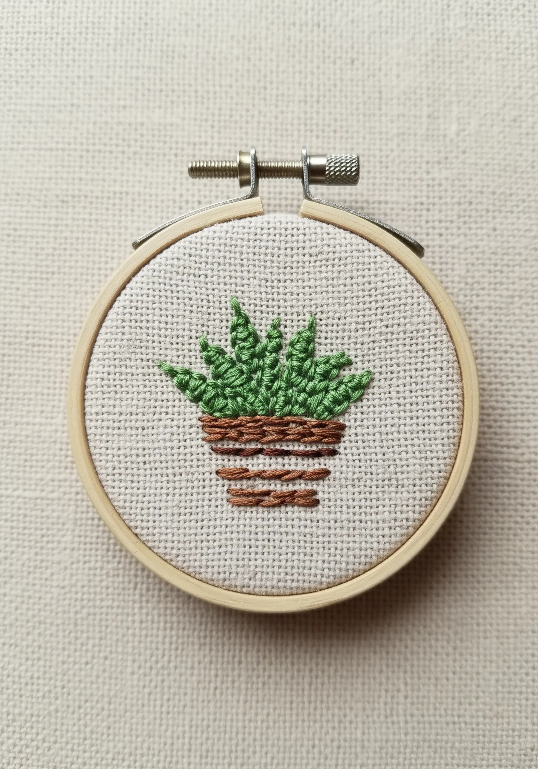 A small embroidered succulent in a brown pot inside a miniature hoop.