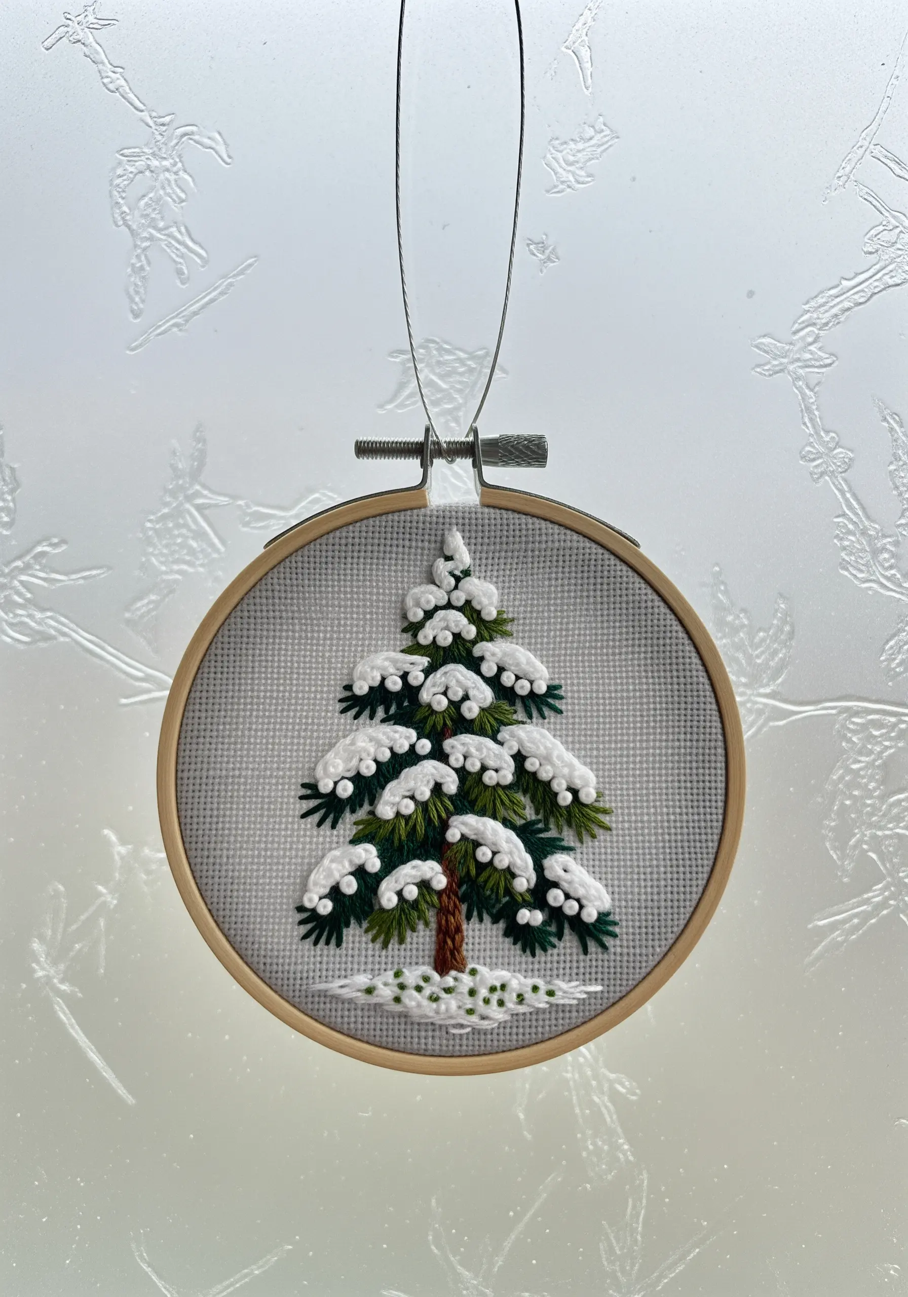 An embroidered pine tree covered in dimensional white stitches that look like snow.