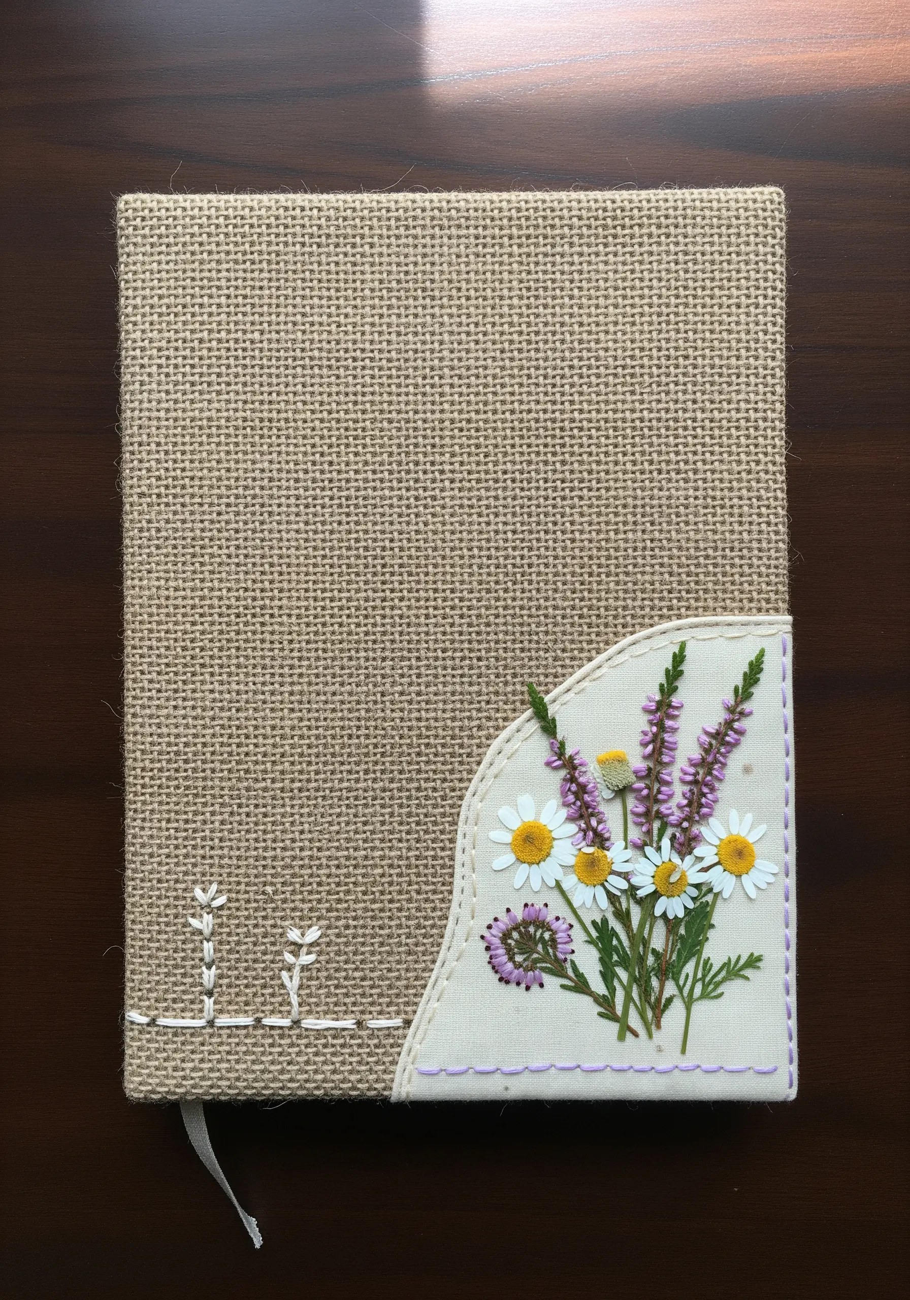 A burlap journal cover with a small cotton pocket holding a bouquet of pressed wildflowers.