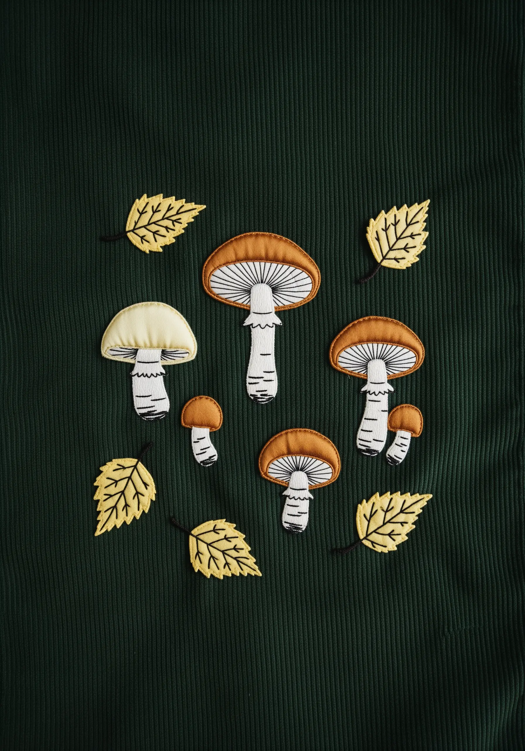 Appliqué and embroidered mushrooms and leaves on a dark green corduroy fabric.