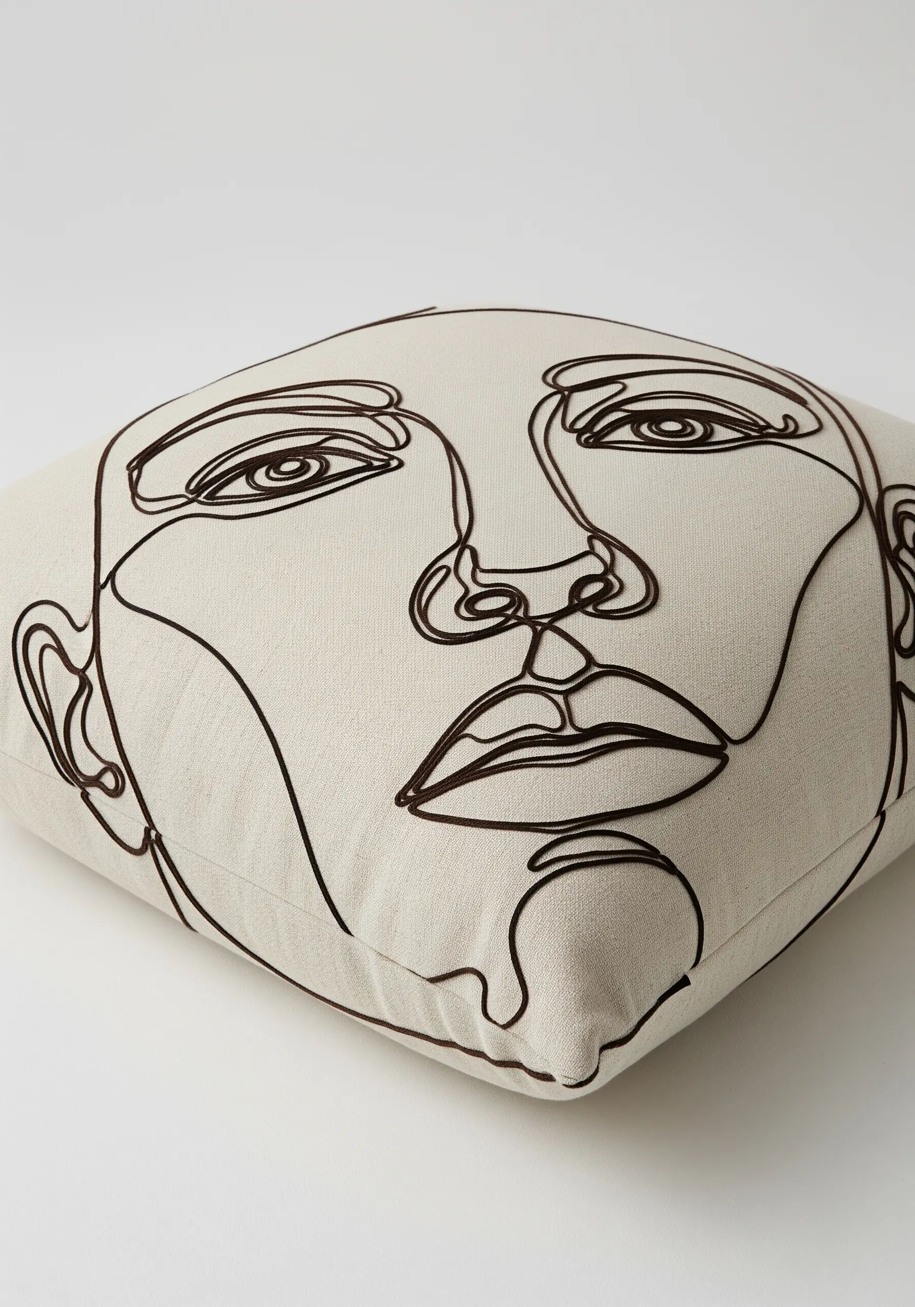 Complex abstract face portrait in continuous black line art on a neutral linen cushion.