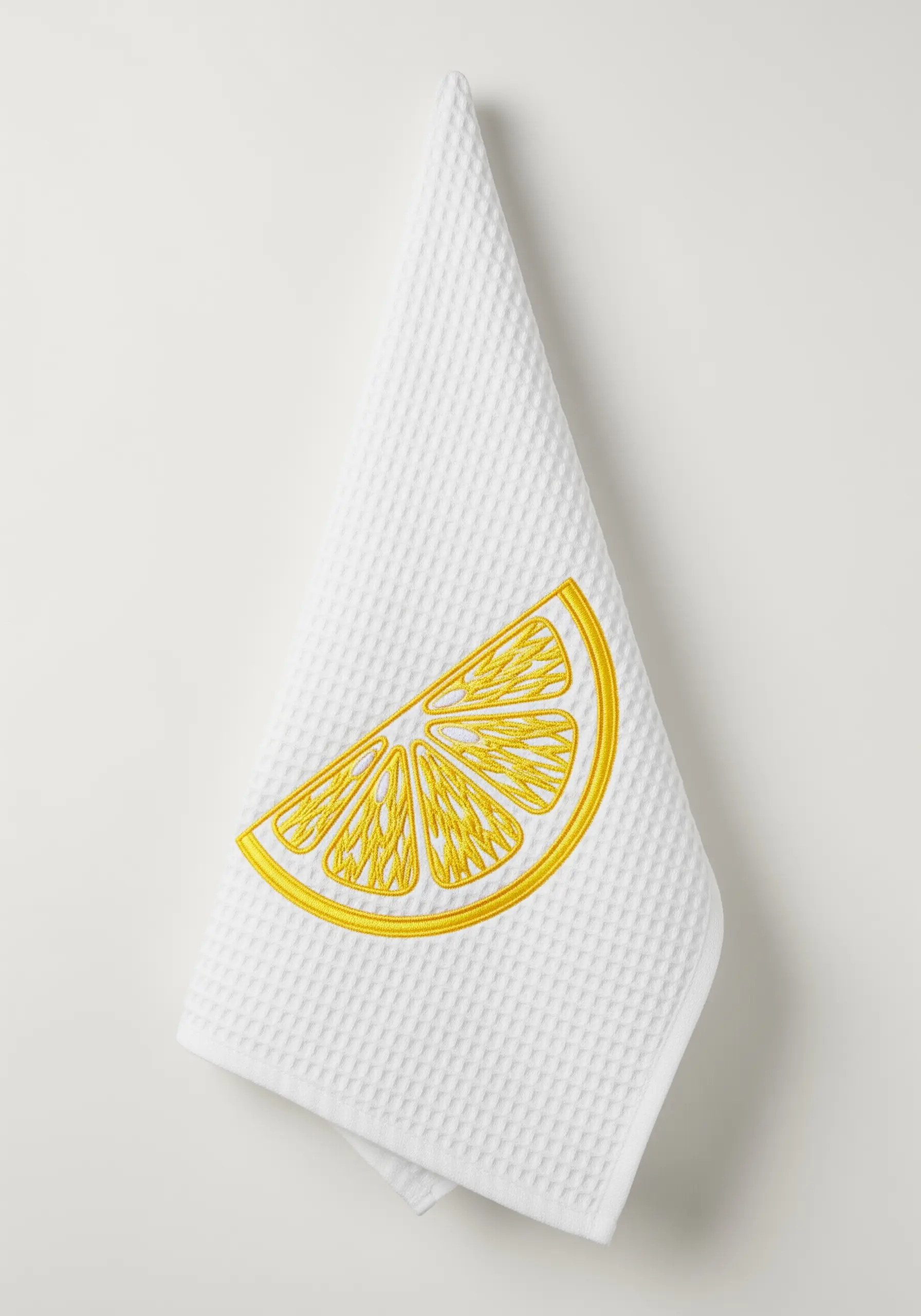 Bright yellow lemon slice embroidered on a white waffle-weave kitchen towel.