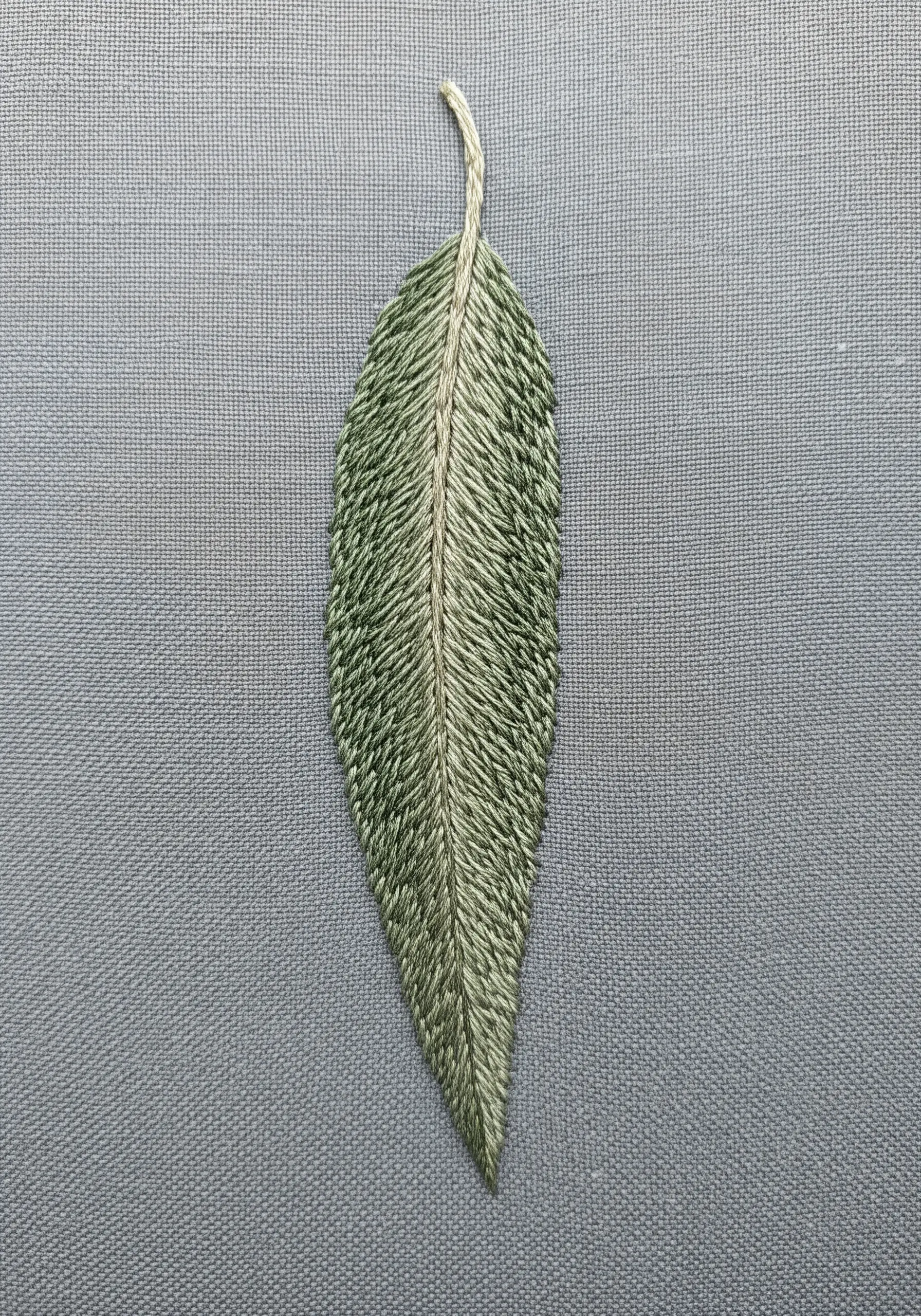 A single, slender leaf stitched entirely with the fishbone stitch in variegated greens.