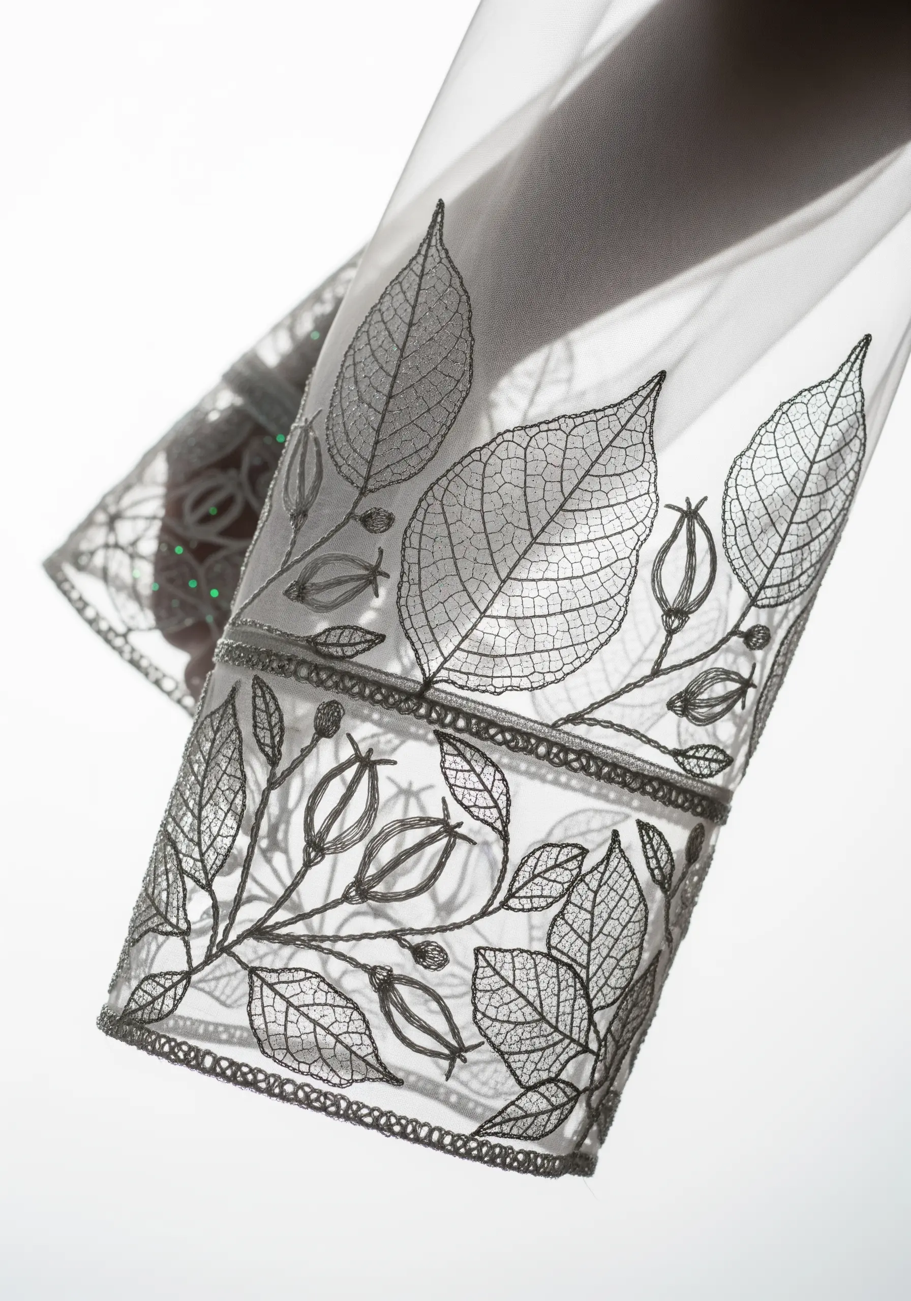 Delicate skeleton leaf embroidery in silver thread on a sheer white sleeve