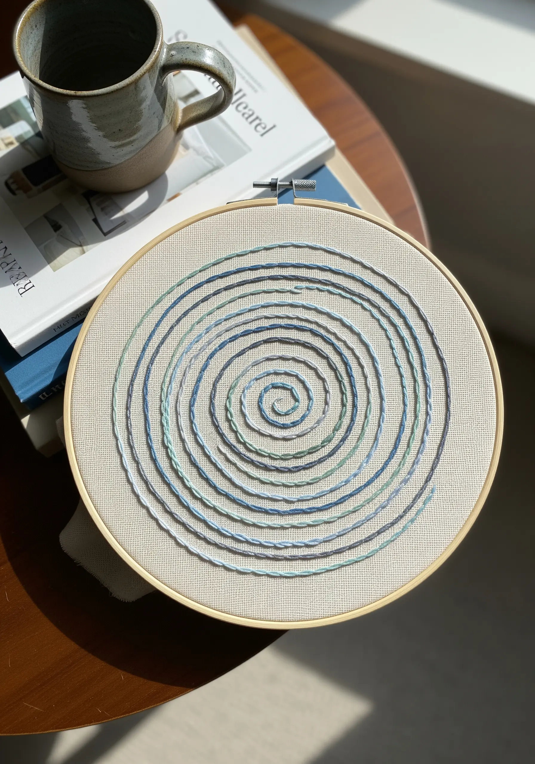 Minimalist hoop art with a spiral stitched in variegated blue and green threads.