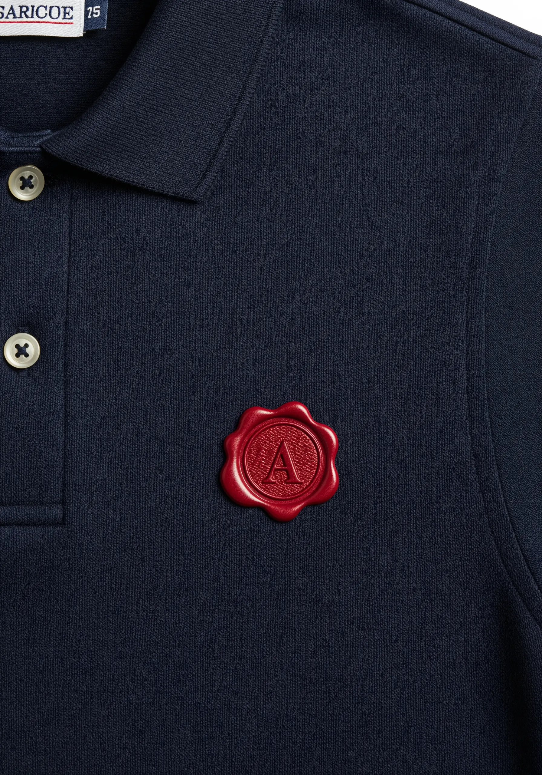 A raised, 3D embroidered red wax seal with the letter 'A' on the chest of a navy blue polo shirt.