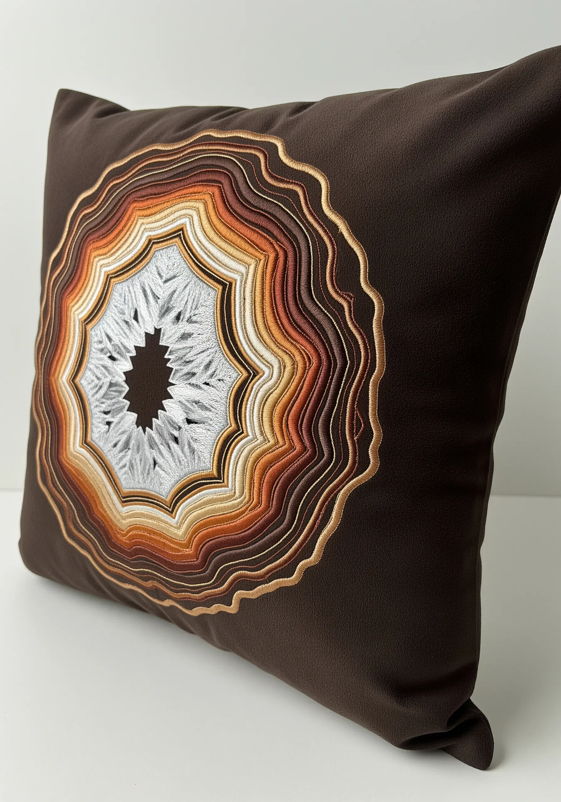 An embroidered agate slice with concentric rings of brown, orange, and white thread.