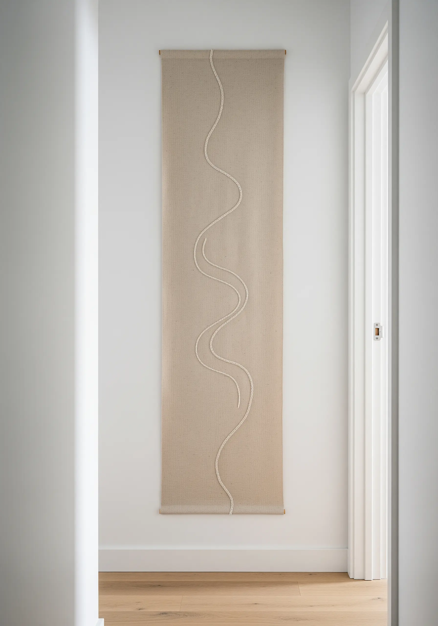 A single, raised meandering line embroidered in white on a long, neutral linen wall hanging.