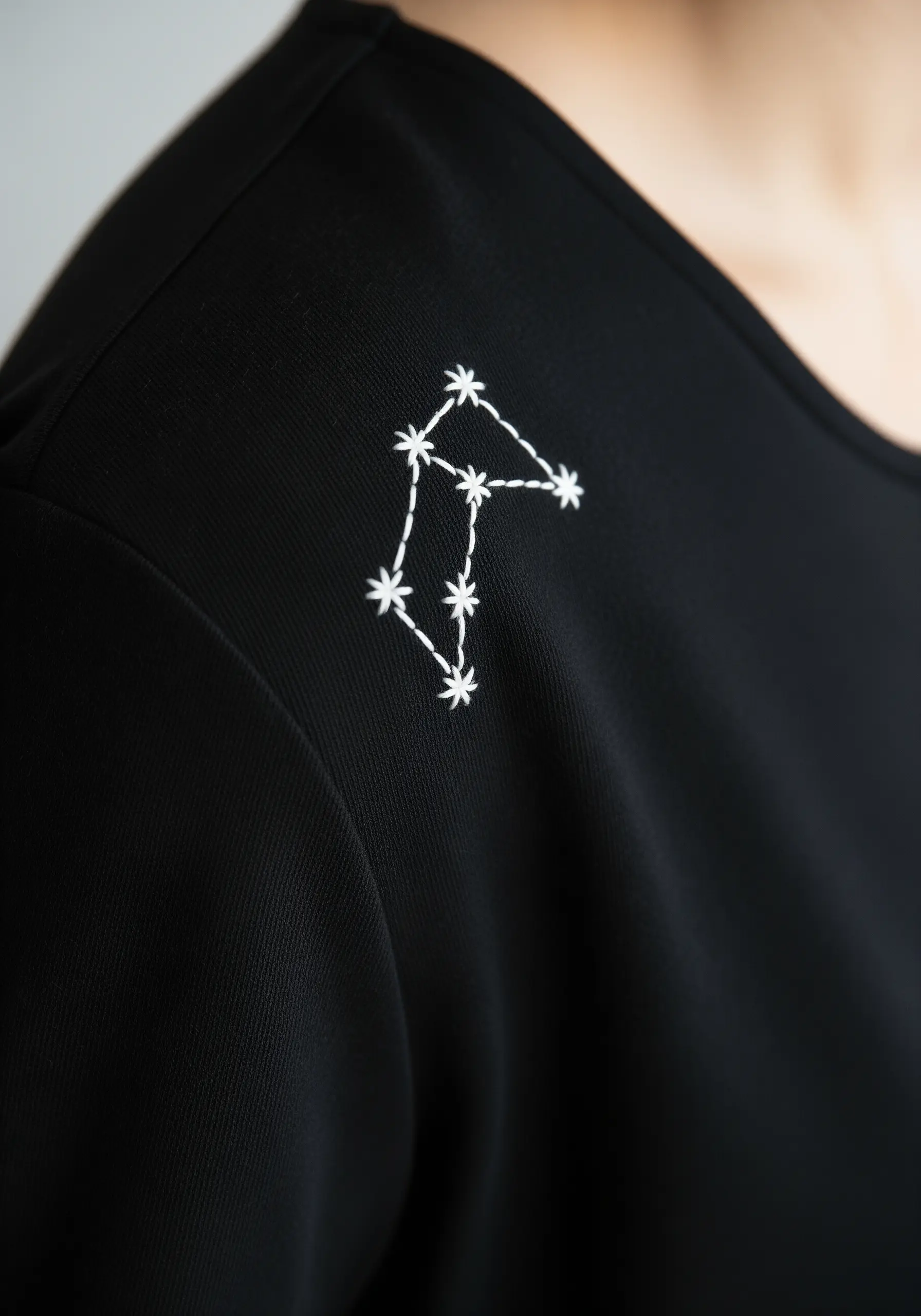 A white embroidered constellation on the shoulder of a black t-shirt.