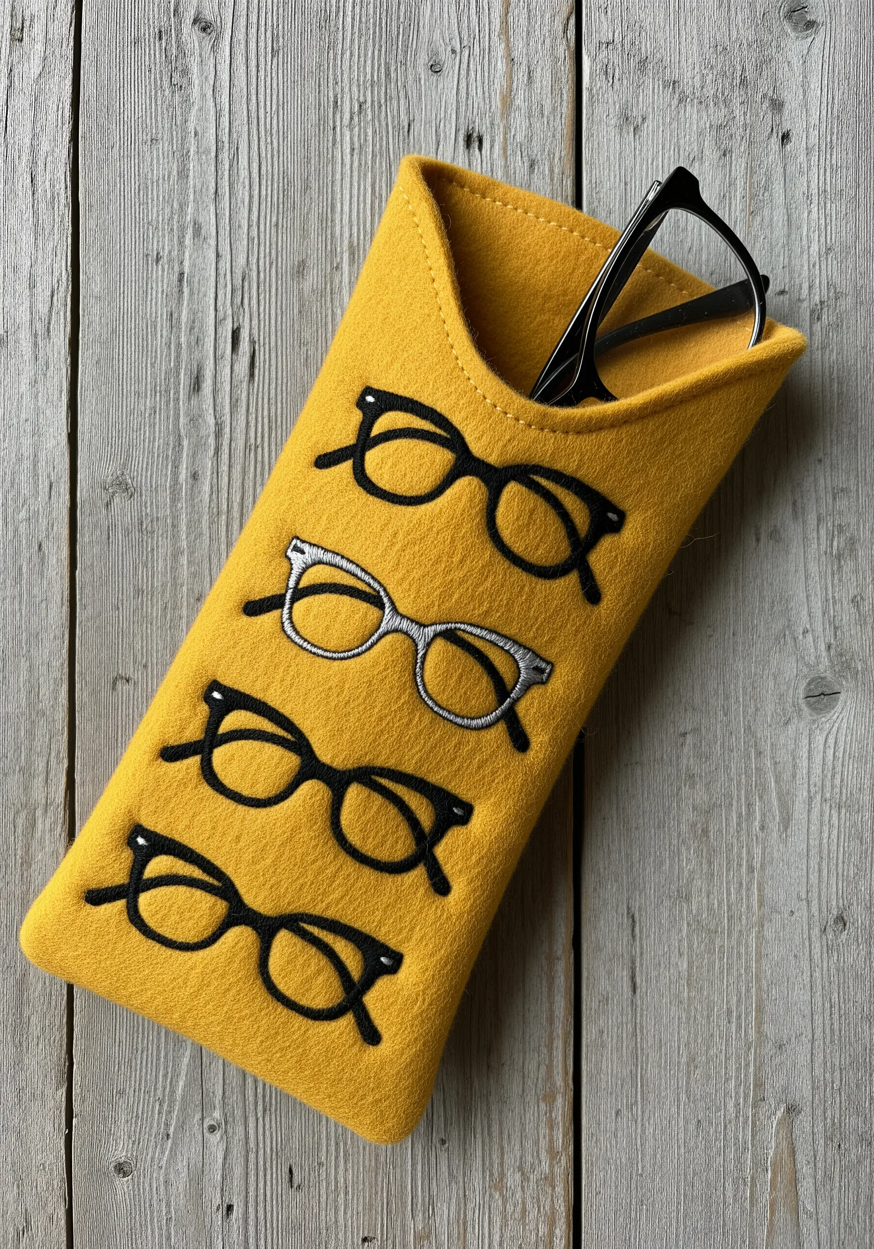 A yellow felt glasses case with four pairs of glasses embroidered in black and white thread.