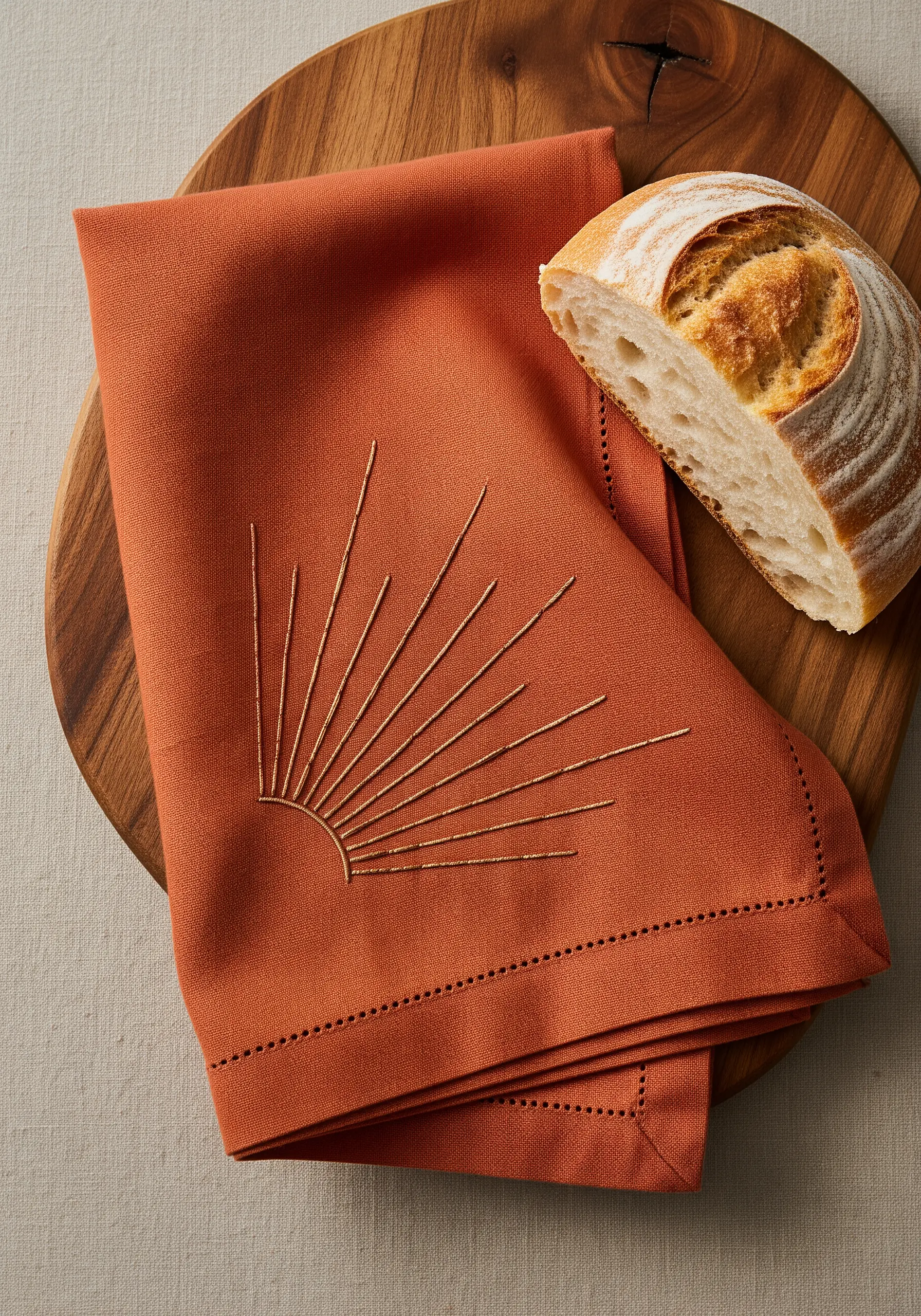 Gold thread sunburst motif with long straight stitches on a terracotta linen napkin.