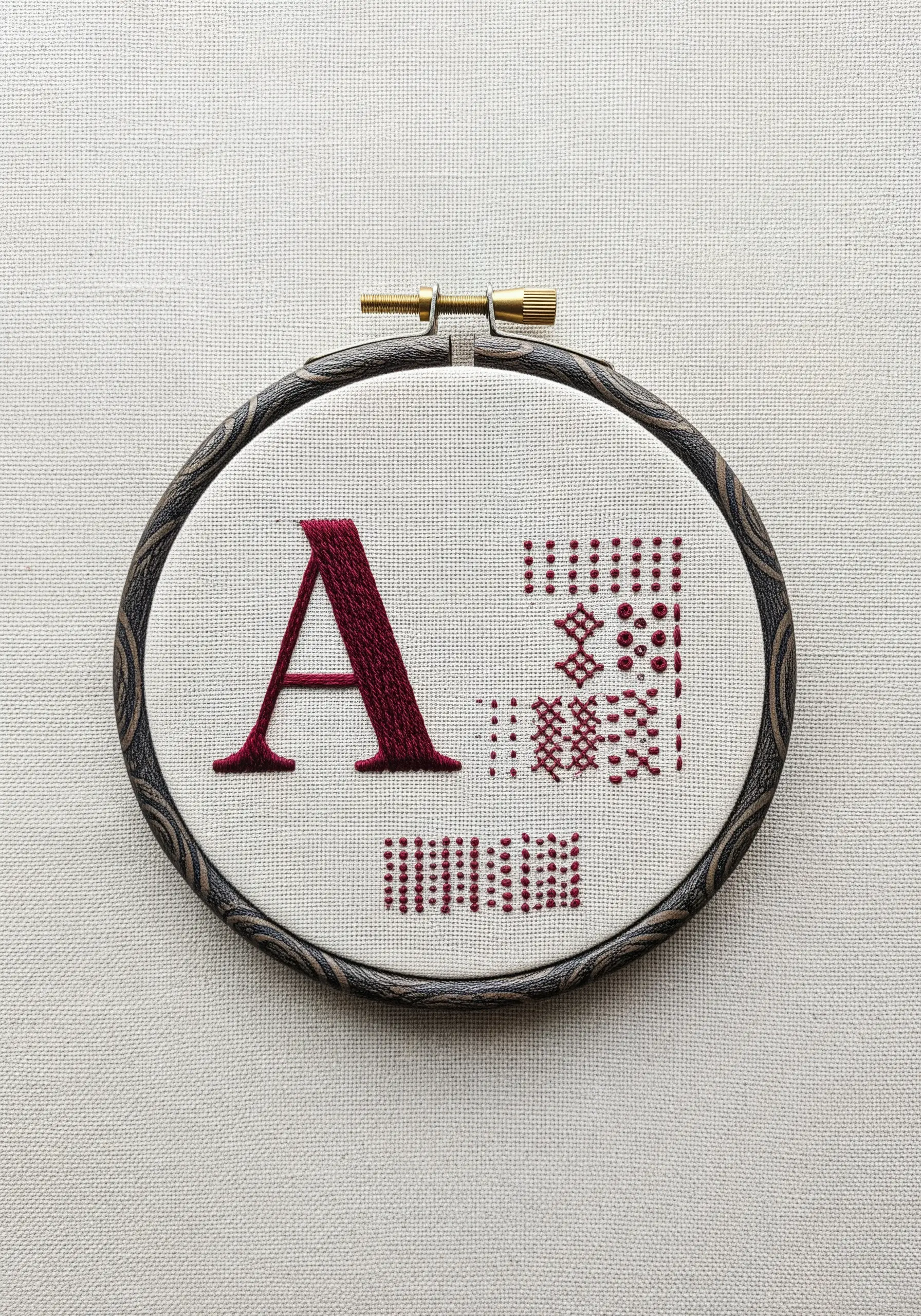 A bold satin stitch letter 'A' next to delicate redwork geometric patterns.