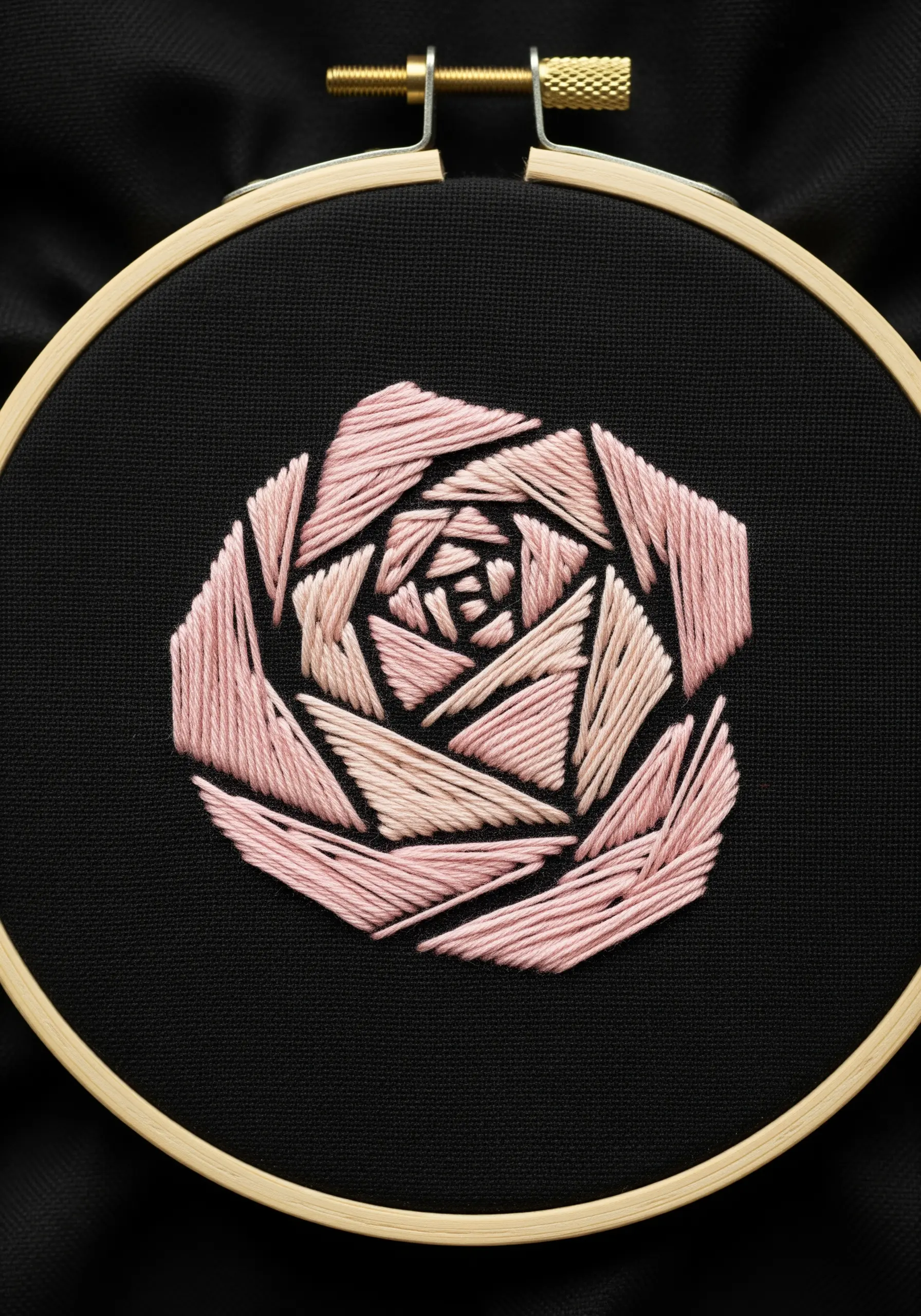 A geometric, faceted pink rose embroidered on black fabric in a hoop.