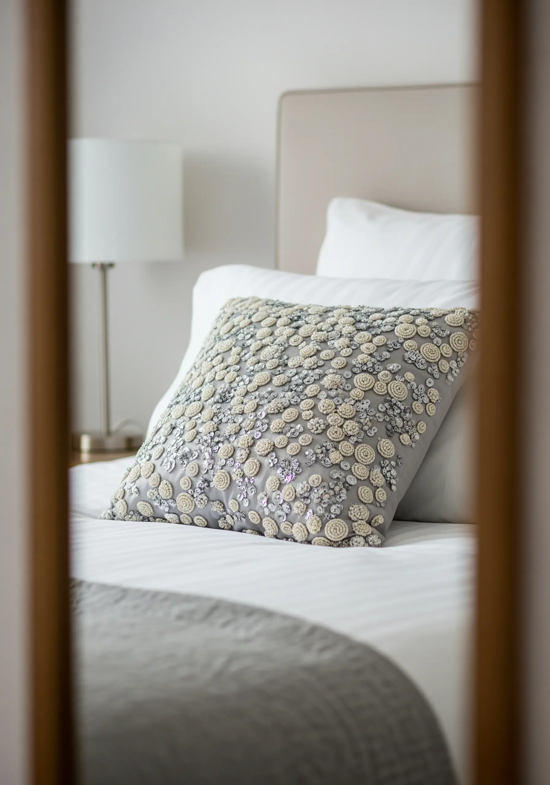 A grey pillow heavily embellished with layered fabric circles, beads, and opalescent sequins.