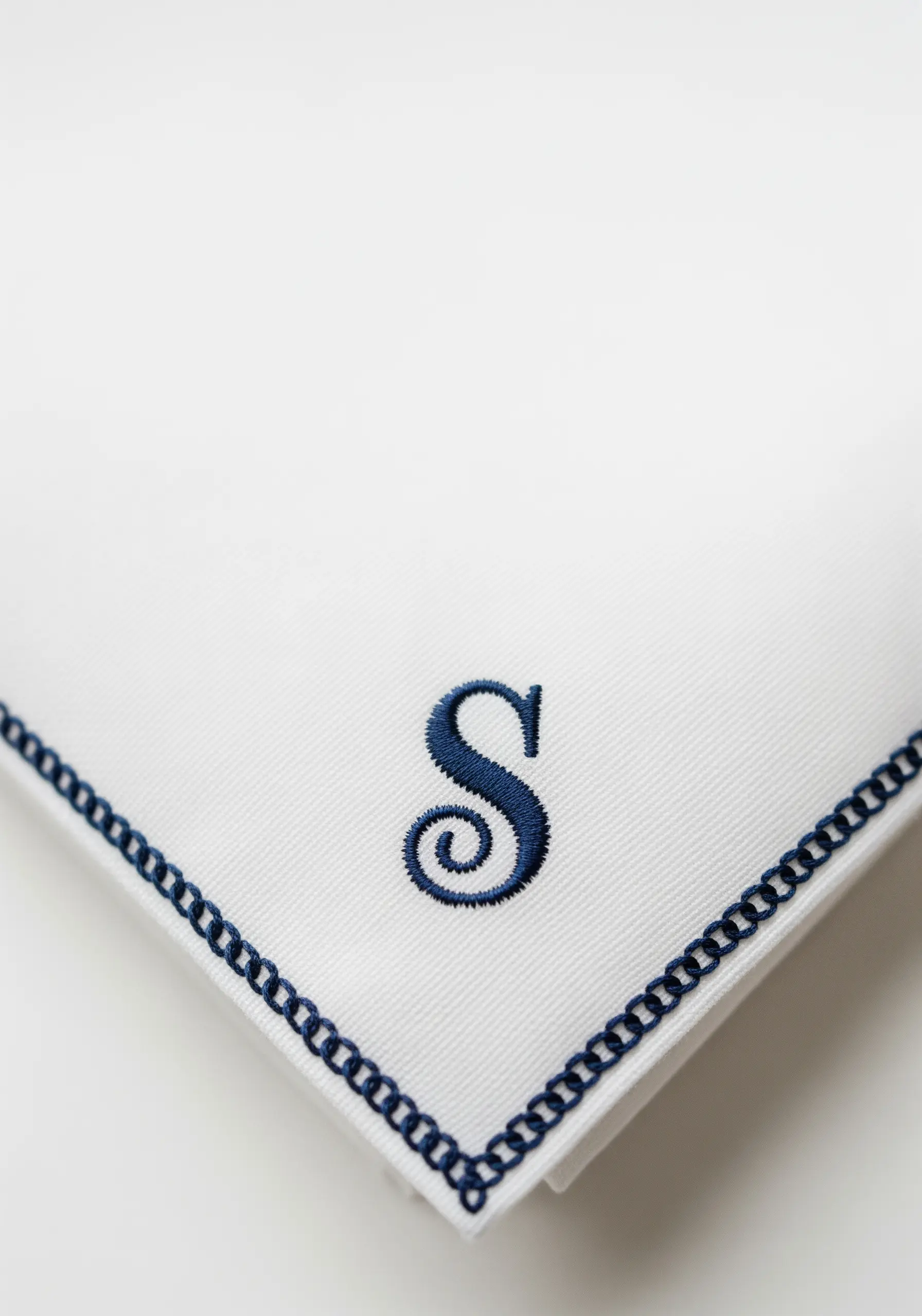 A navy blue padded satin stitch monogram 'S' on a crisp white handkerchief.