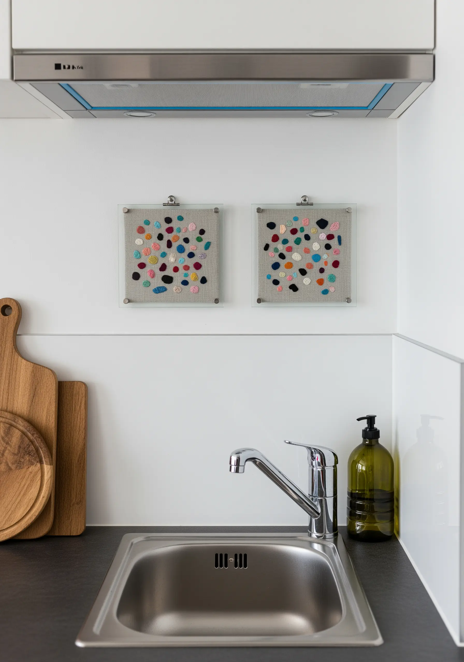 Two small frames with colorful, pebble-like shapes stitched on neutral linen.