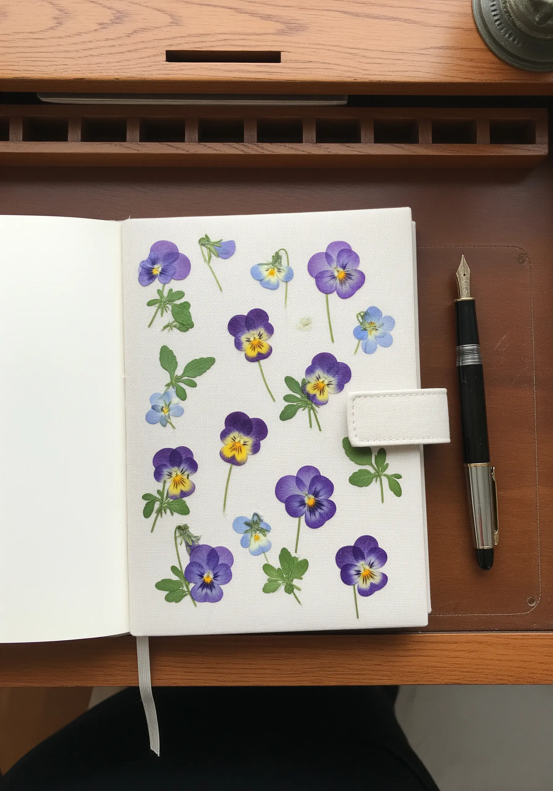 A fabric journal cover decorated with small, scattered embroidered pansies and leaves.