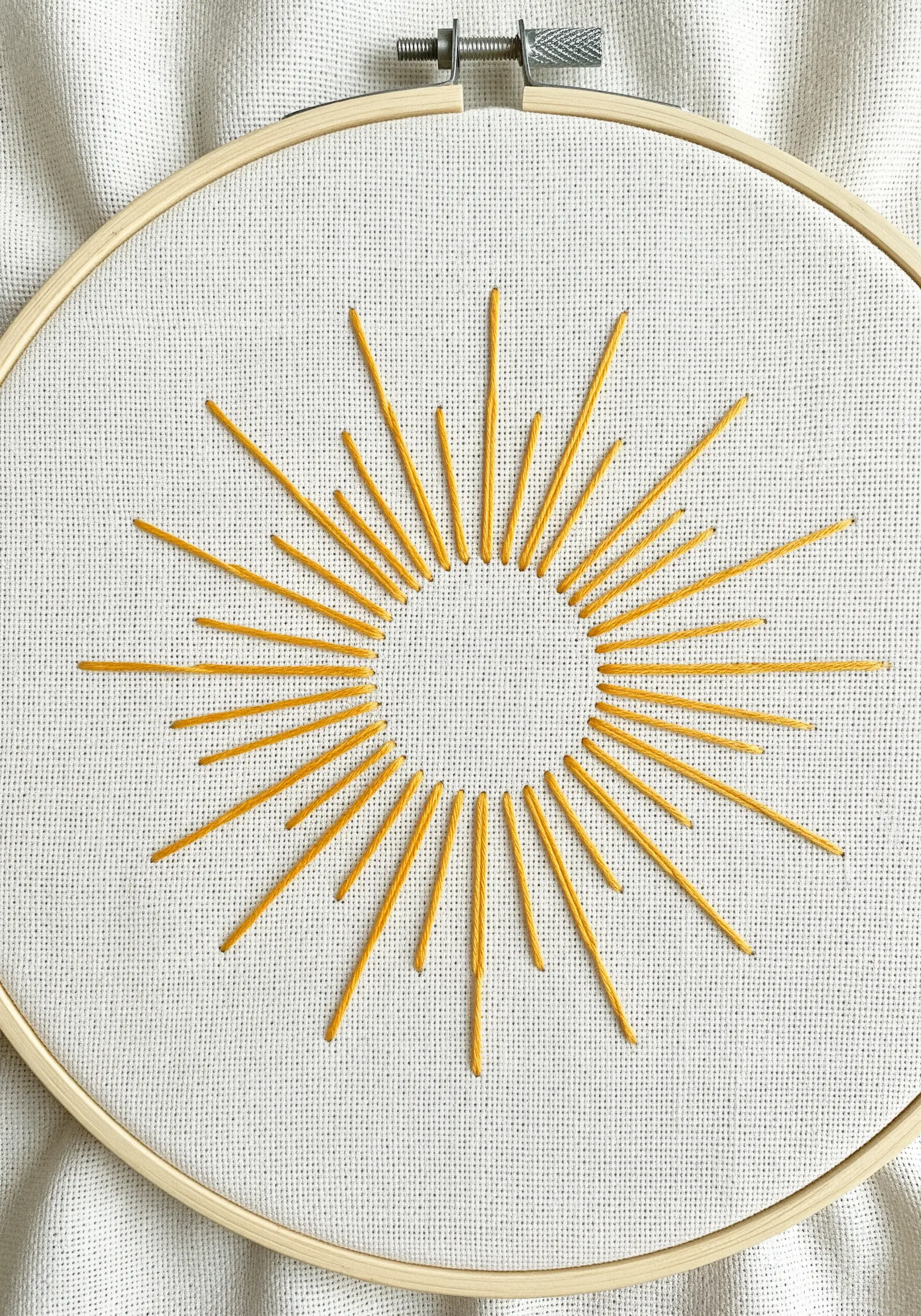 A stylized sun stitched with golden yellow straight stitches of varying lengths on white fabric.