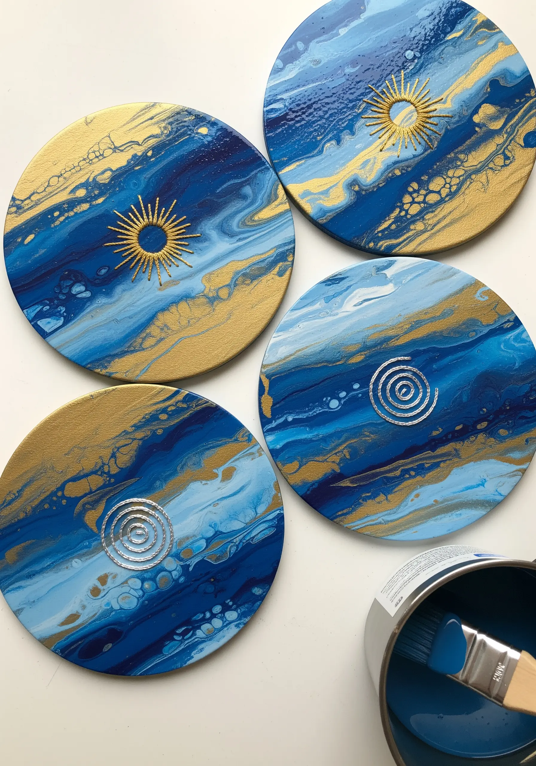 Blue and gold acrylic pour coasters embellished with minimalist sun and spiral embroidery.