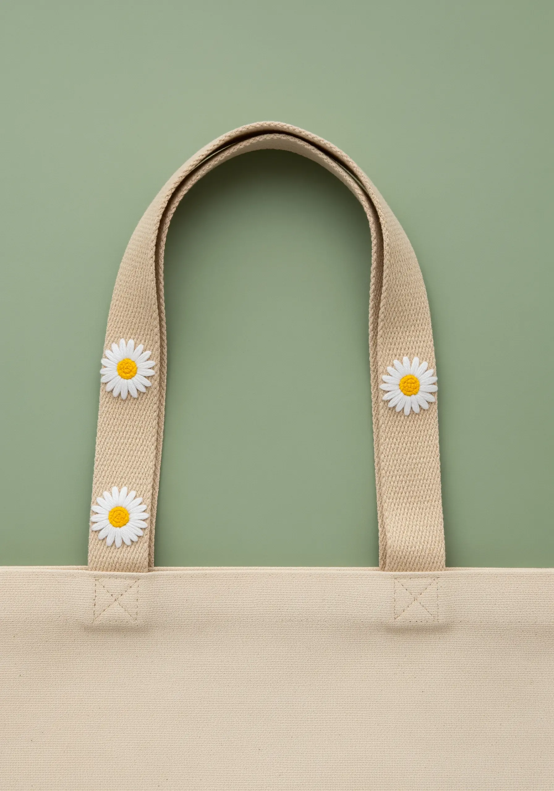 Three embroidered daisy motifs stitched onto a canvas tote bag strap.