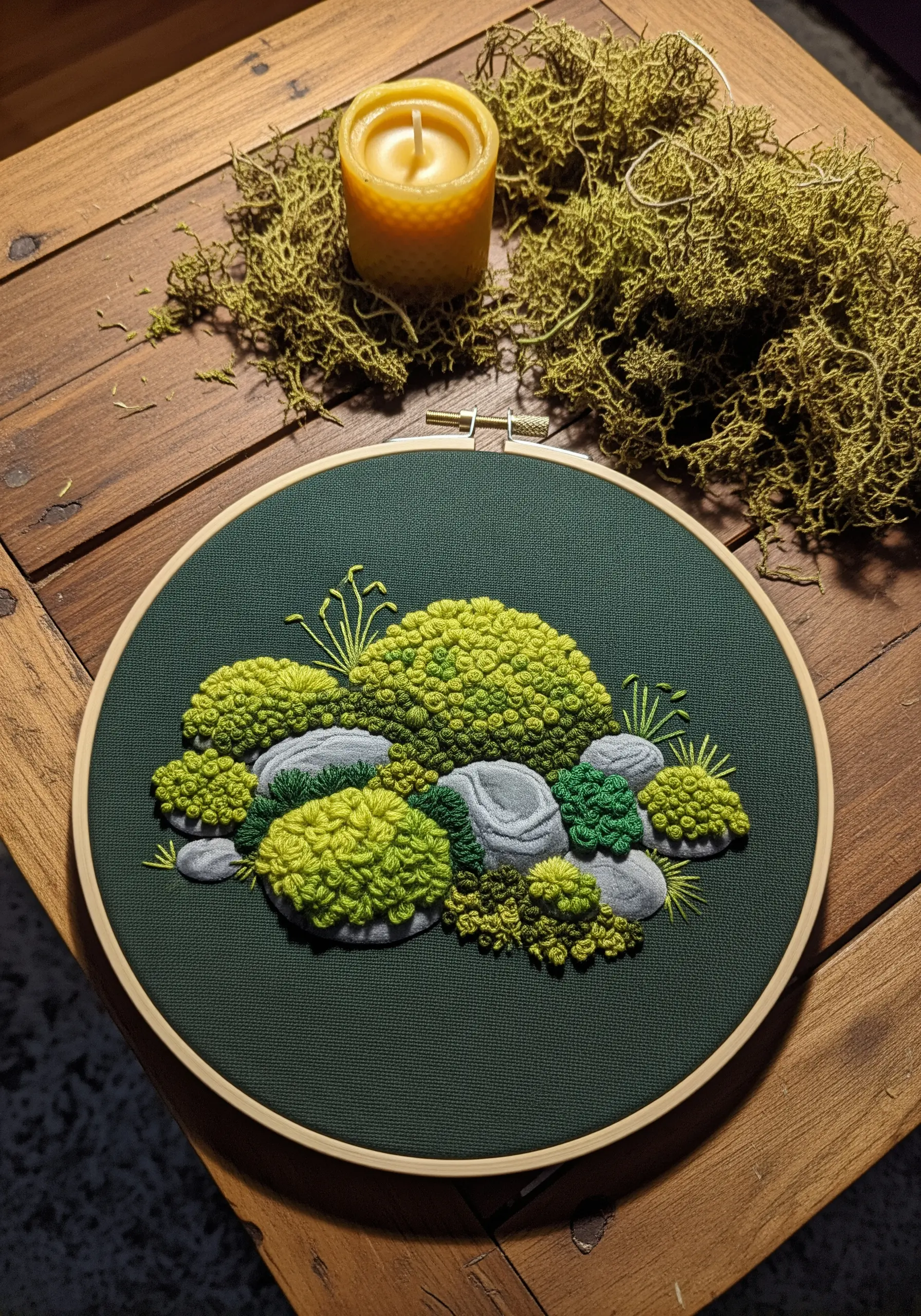 Embroidery hoop art with 3D moss made from French knots on gray stones.