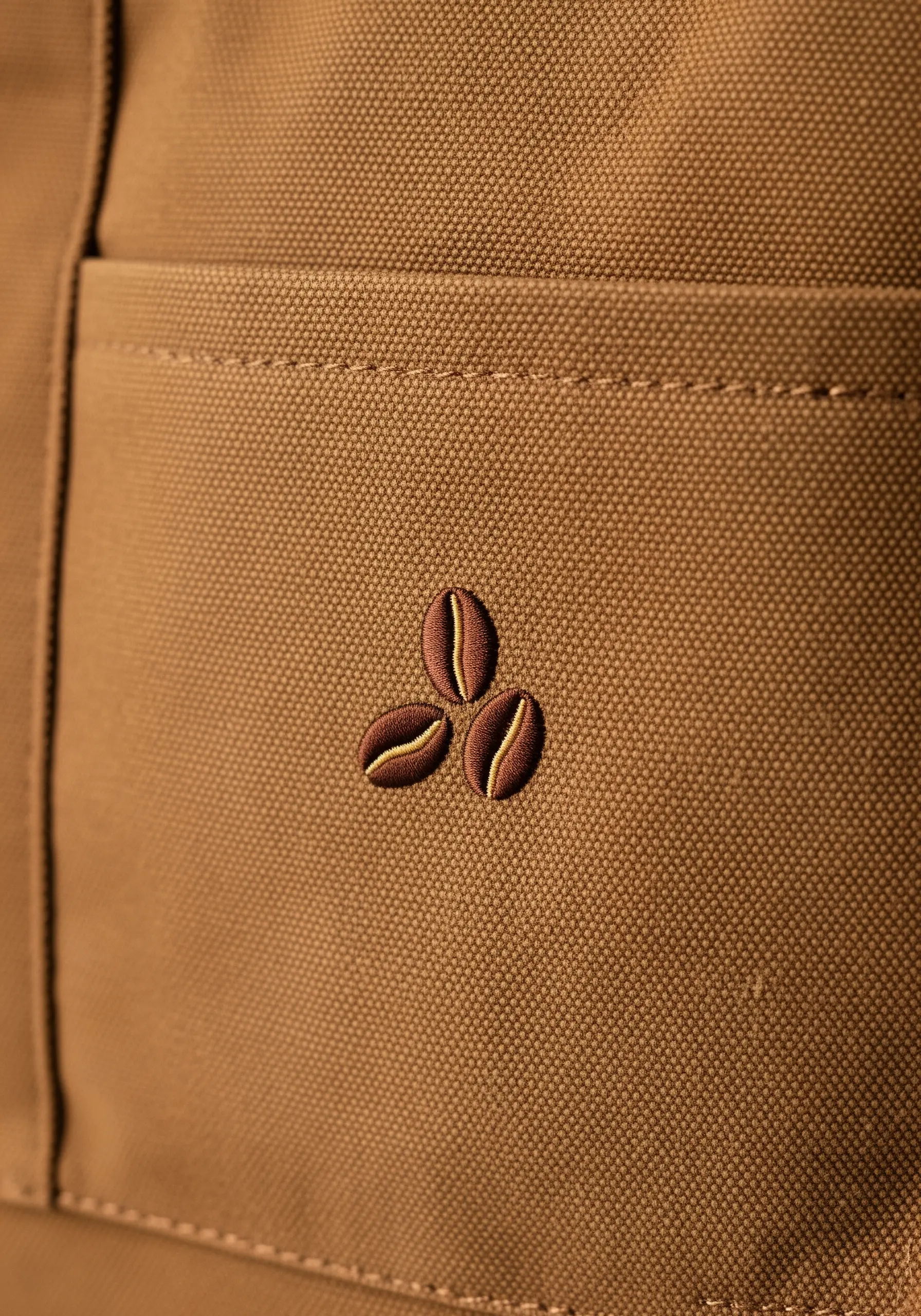 Three small, rounded coffee beans embroidered on a pocket using padded satin stitch.