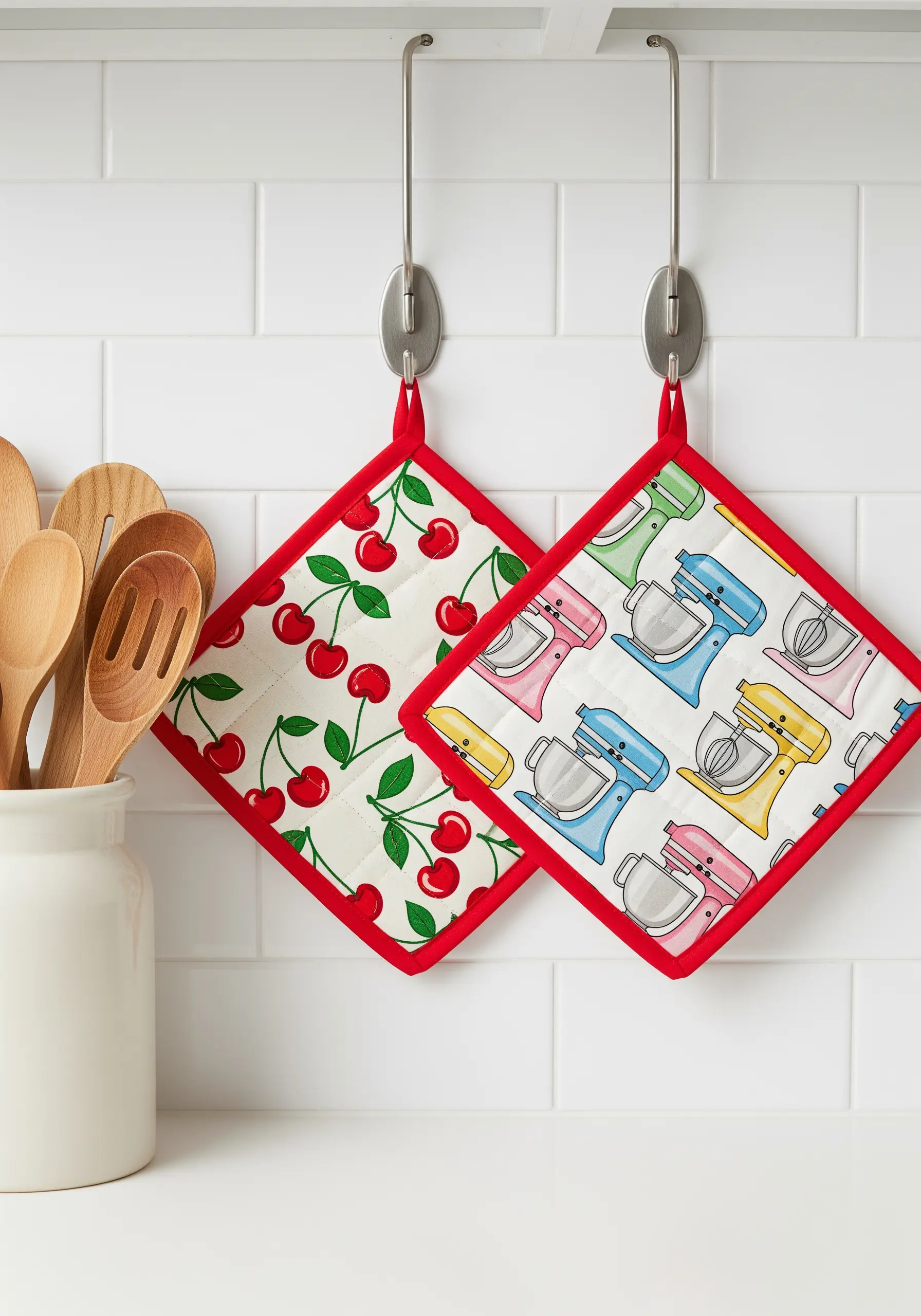 Two patterned, quilted potholders with red bias tape binding hanging on hooks.