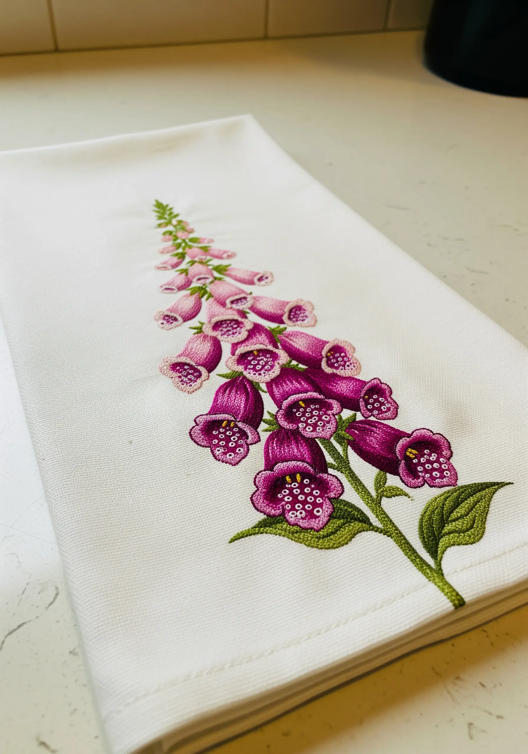 A stalk of embroidered pink and purple foxglove flowers on a white linen towel.