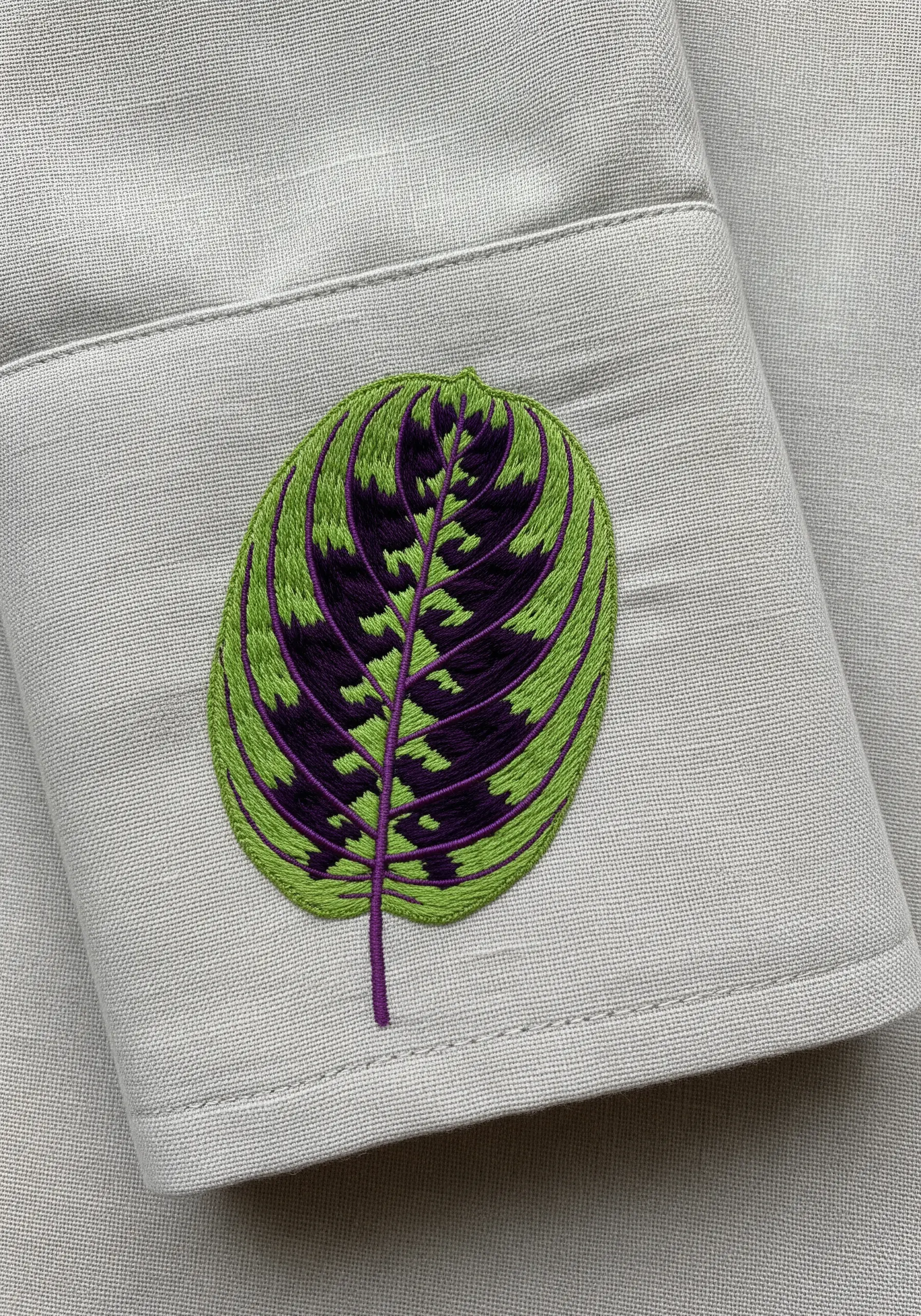 A simplified, graphic Calathea leaf with purple and green blocks embroidered on a shirt cuff.