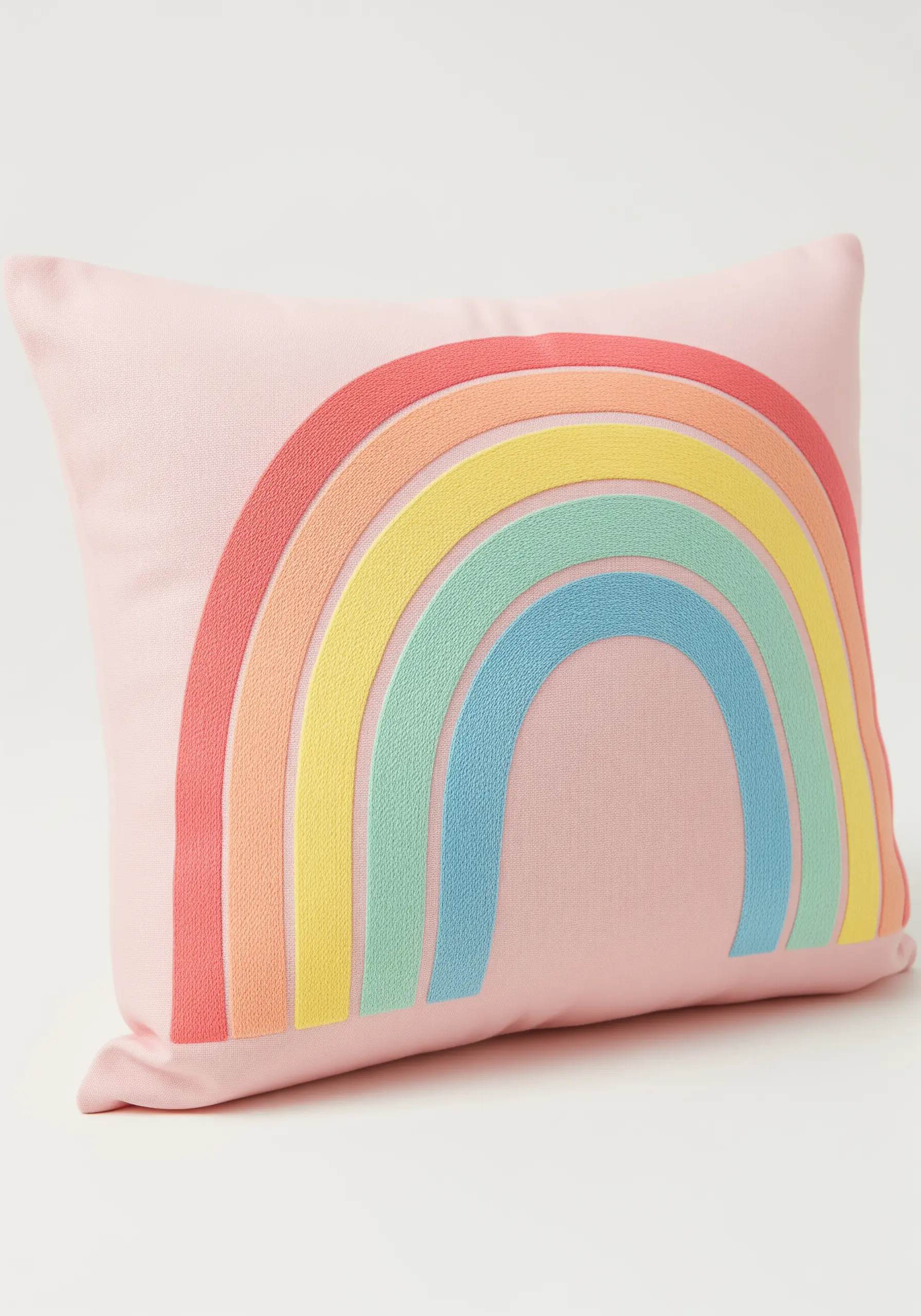 A pastel rainbow with raised satin stitch arcs embroidered on a light pink cushion.