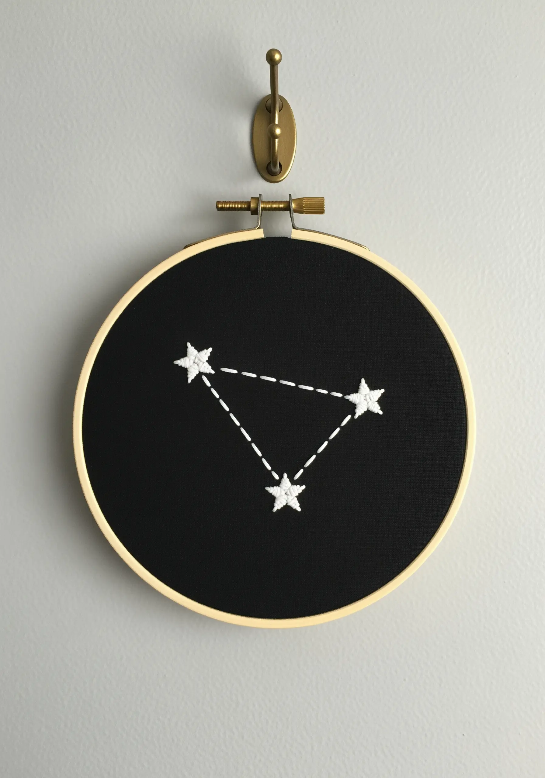 A simple three-star constellation stitched in white thread on a black fabric background.