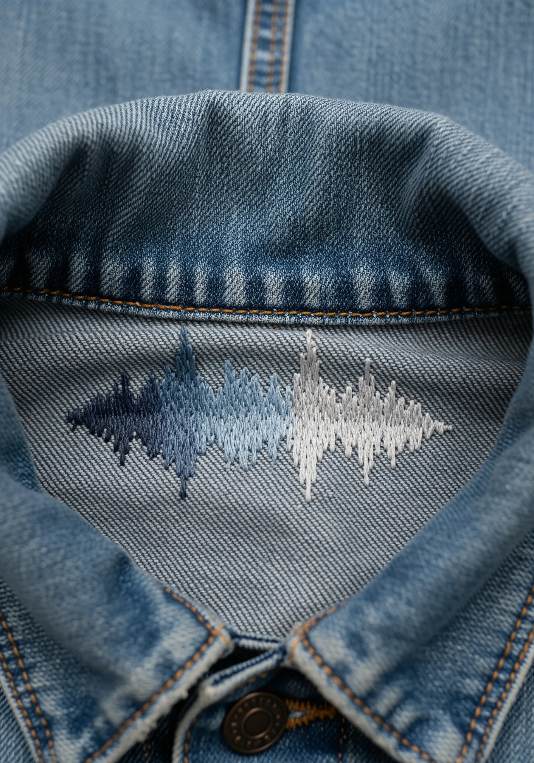 An embroidered soundwave pattern in a blue-to-white gradient on the inside collar of a denim jacket.