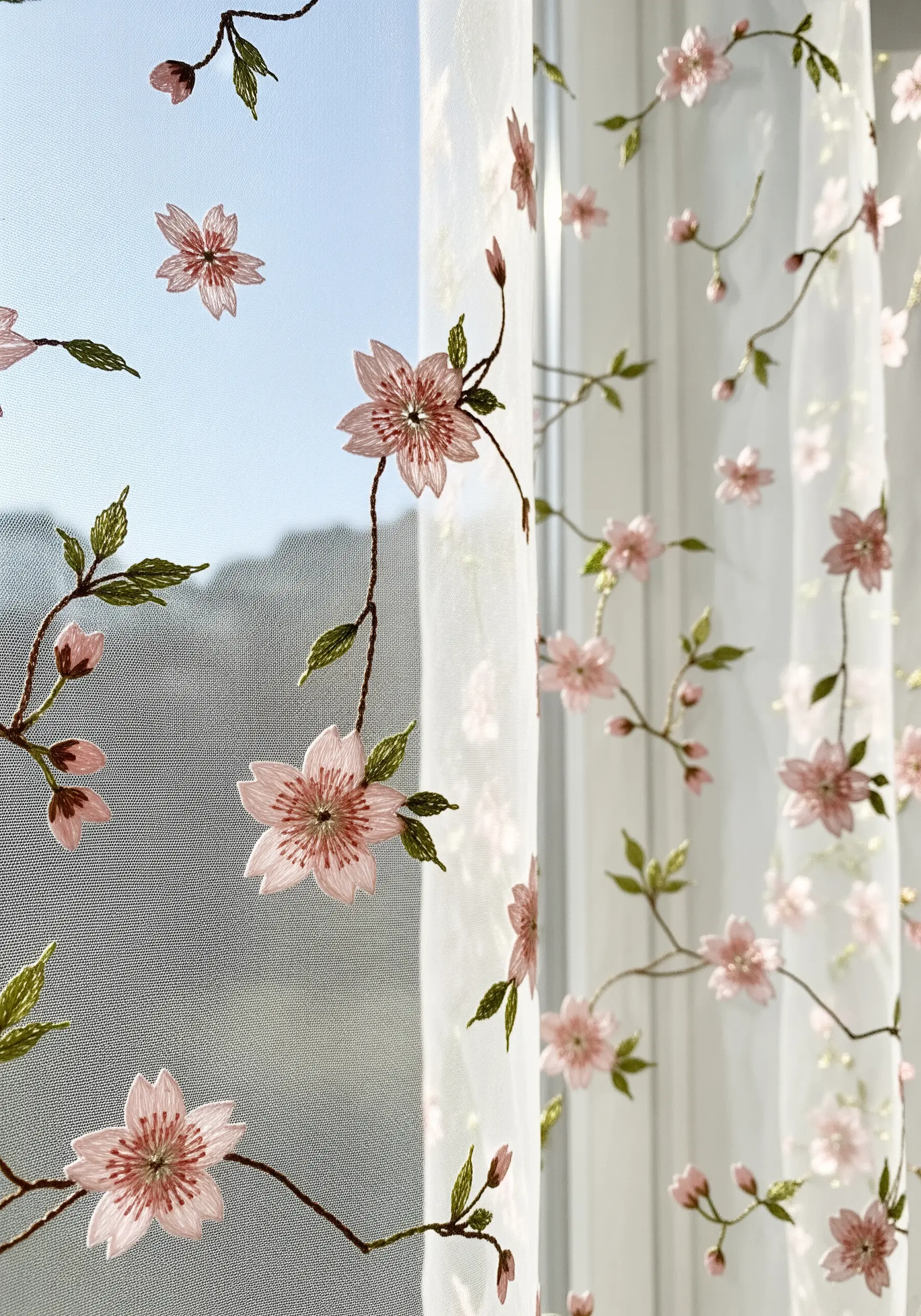 Delicate pink cherry blossoms embroidered on a white sheer curtain, with light filtering through.